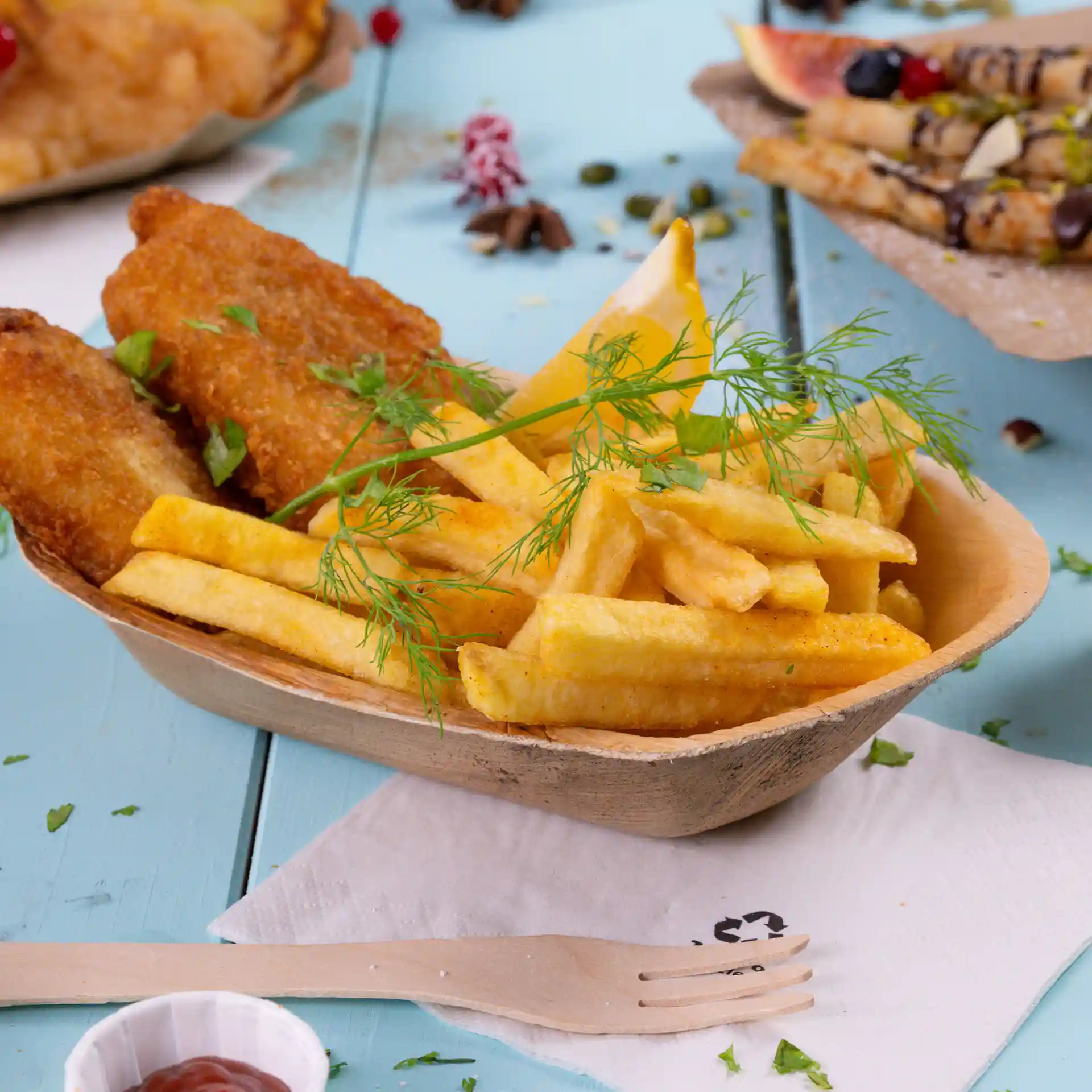 Bateau en feuille de palmier rempli de frites, deux morceaux de poisson frit, un quartier de citron et une branche d'aneth.