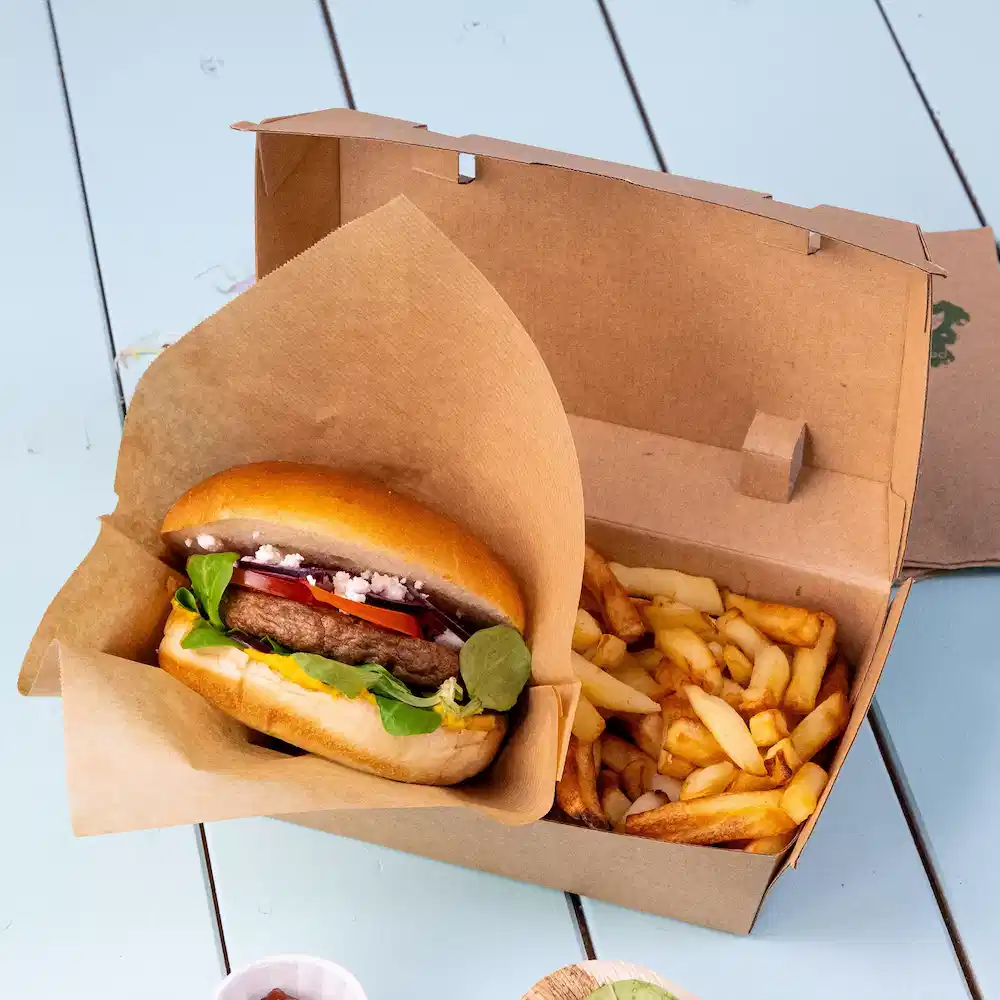 Burger avec garnitures placé dans une boîte à emporter à côté d'une portion de frites.