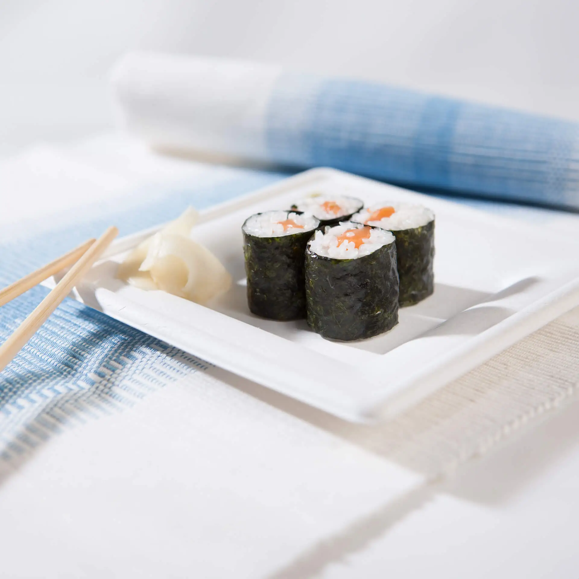 Assiette carrée en canne à sucre avec des sushi et du gingembre mariné, sur une table bleue et blanche.