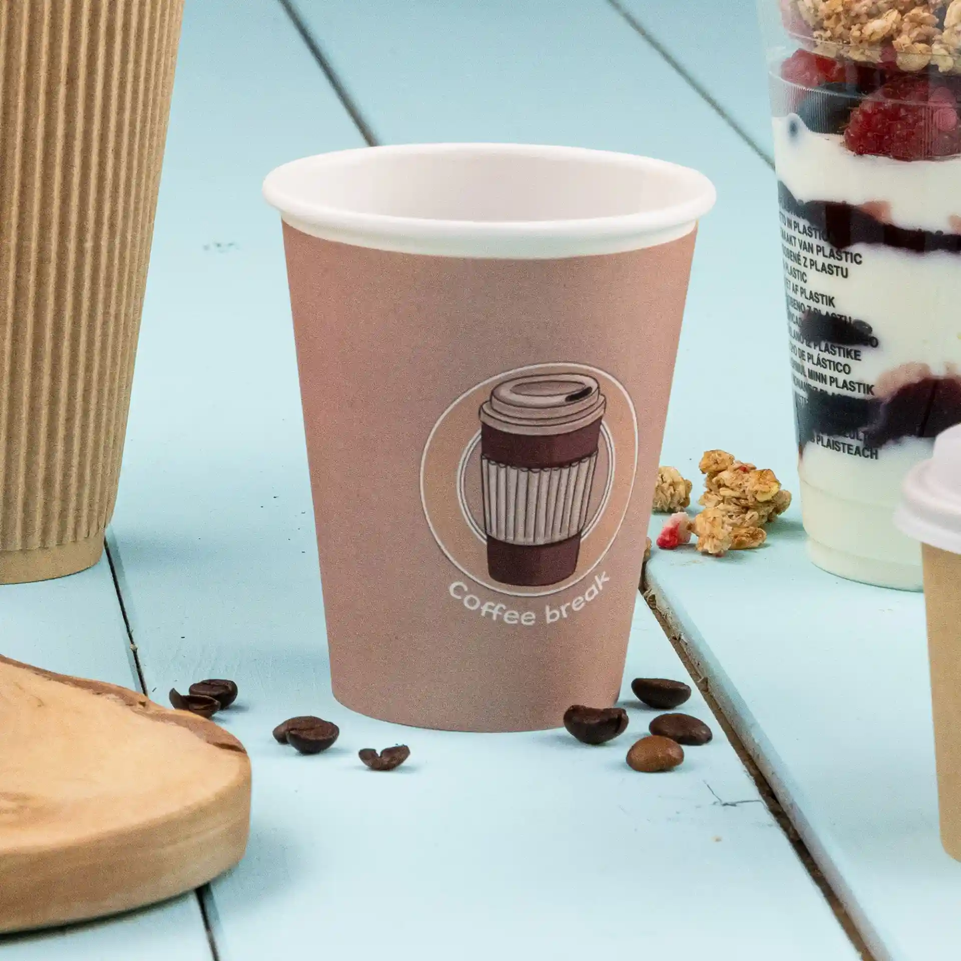 Gobelet en papier brun avec un design de café imprimé et du texte, placé sur une surface bleue avec des grains de café à proximité.