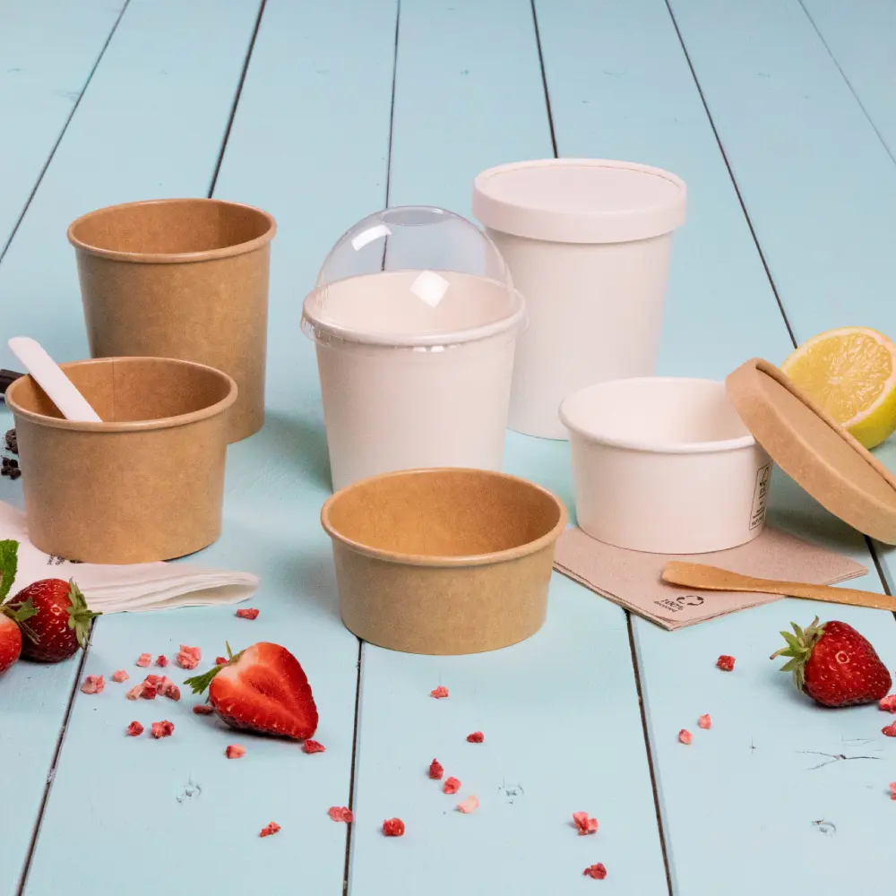 Contenants pour desserts à emporter de différentes tailles, en papier et en plastique, entourés de fraises et de citron.