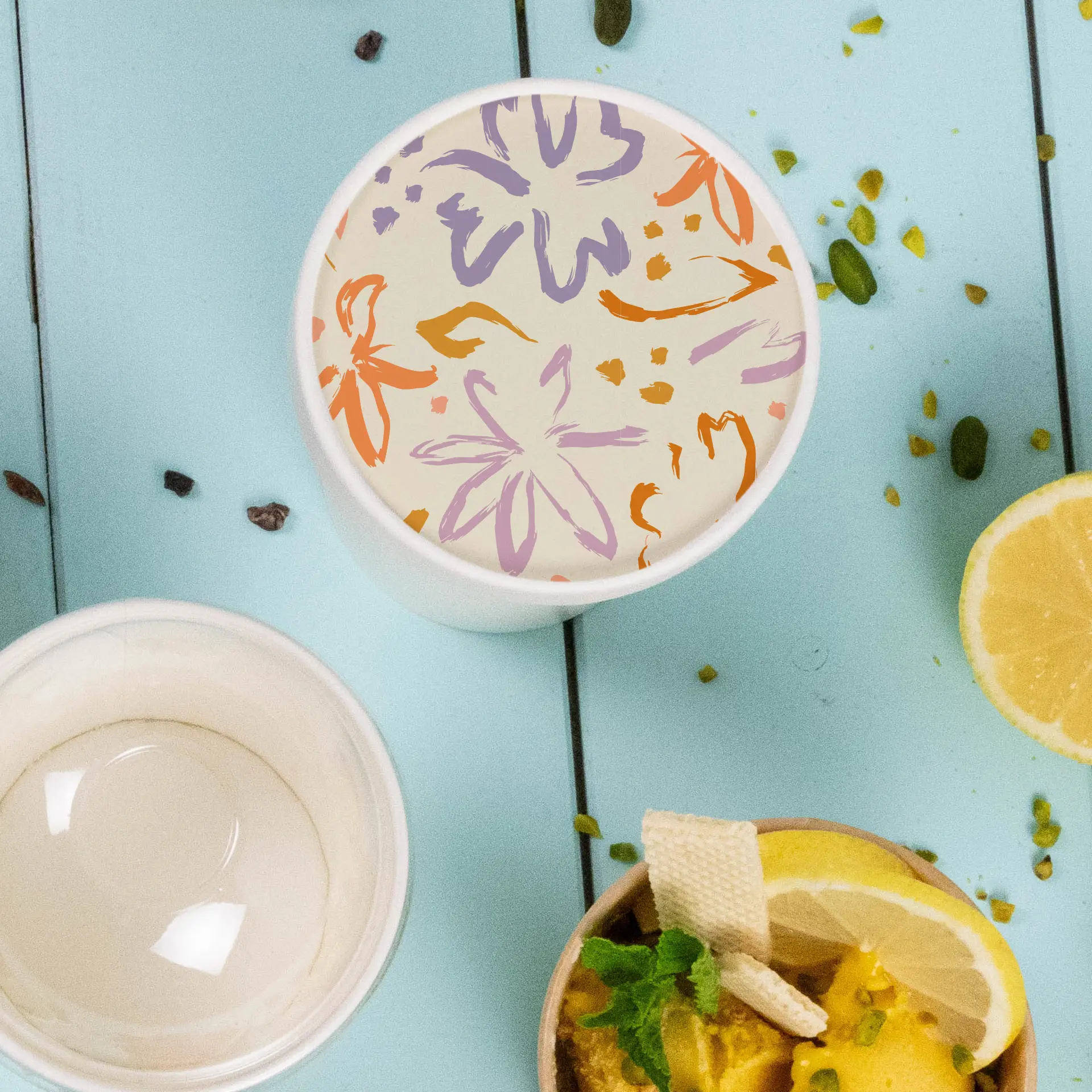 Couvercle imprimé sur mesure pour un pot de crème glacée avec un motif floral, placé sur une surface bleue avec des aliments à proximité.