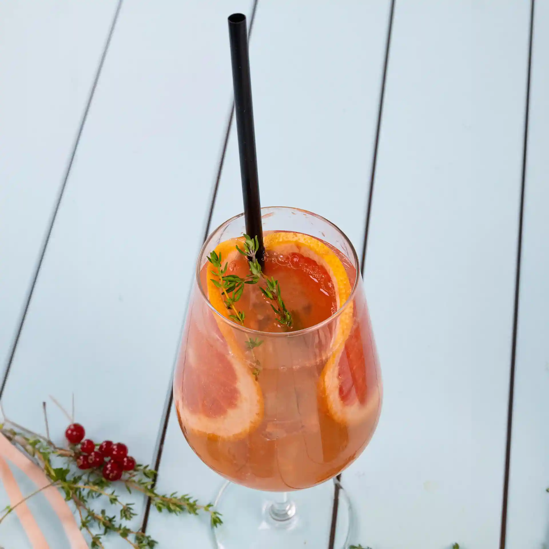Image d'un verre transparent rempli d'une boisson, garni de tranches d'orange et de thym, avec une paille noire.