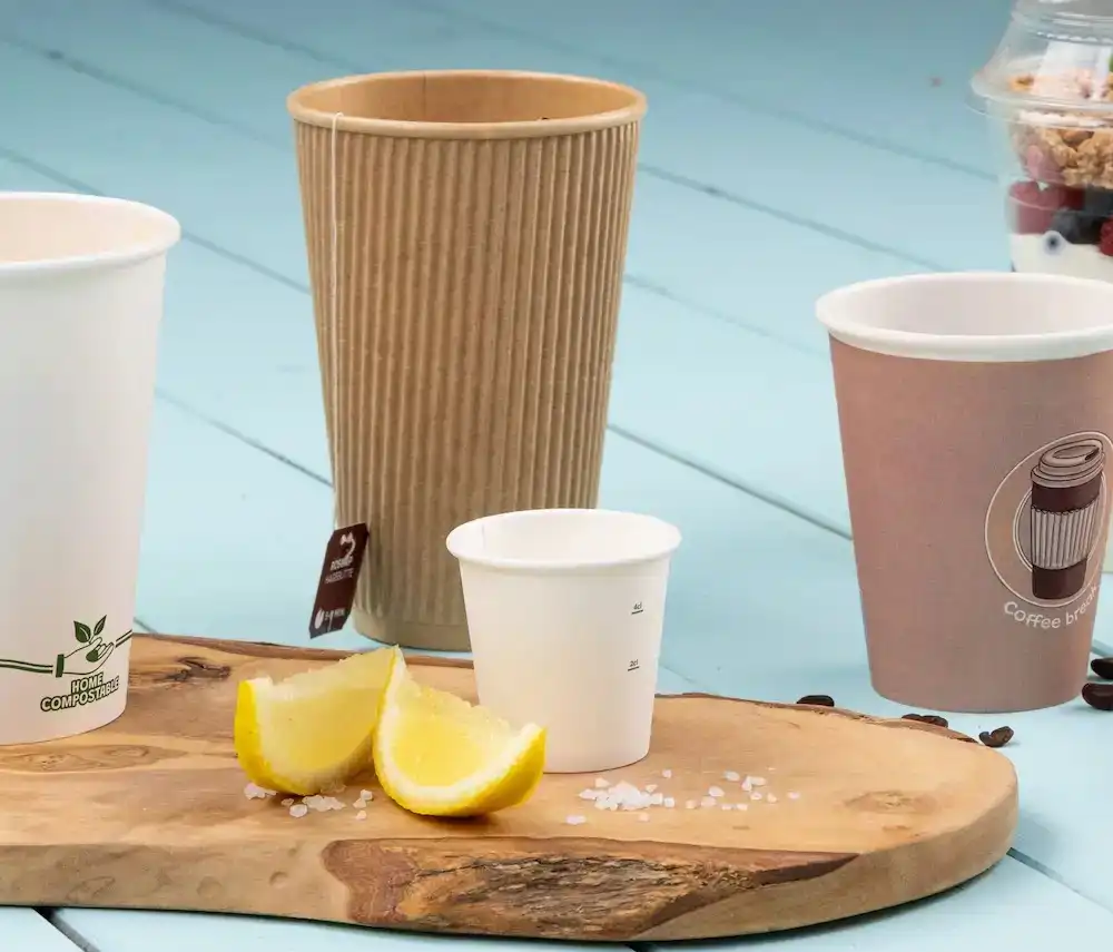 Gobelets en papier assortis sur une surface en bois avec des quartiers de citron et des cristaux de sel.