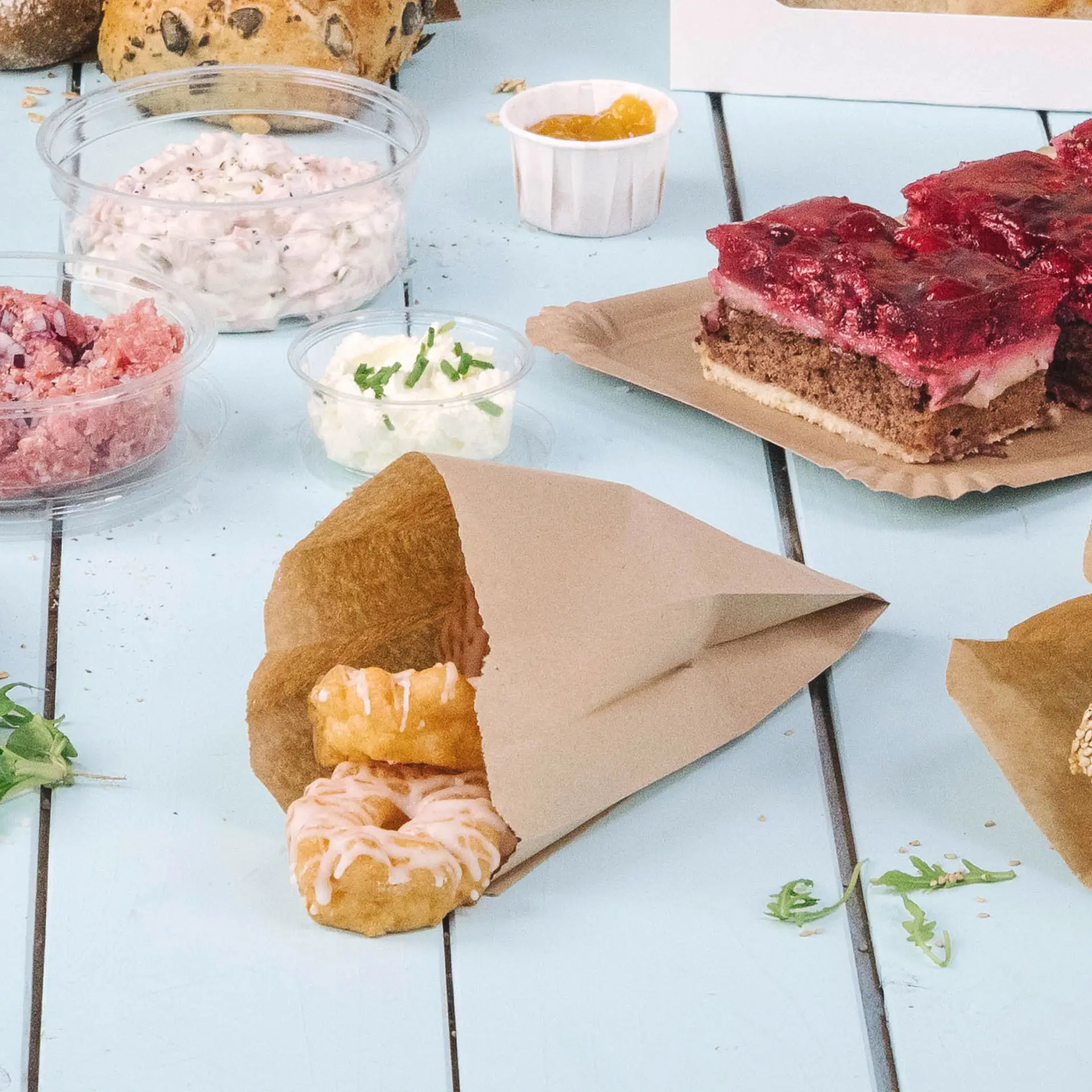 Sac en papier brun avec deux donuts glacés partiellement visibles ; divers contenants alimentaires en arrière-plan.