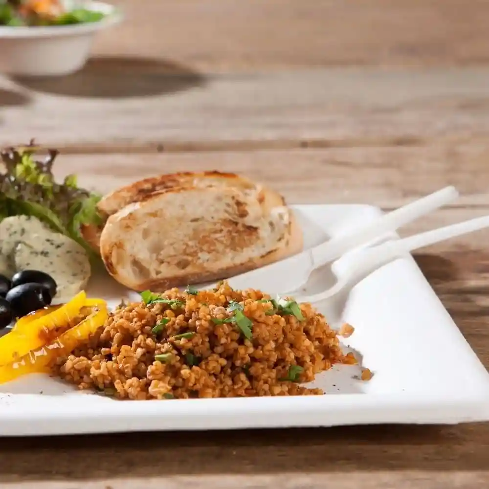 Assiette de boulgour, légumes grillés, olives, une tranche de pain et une salade sur une table en bois.