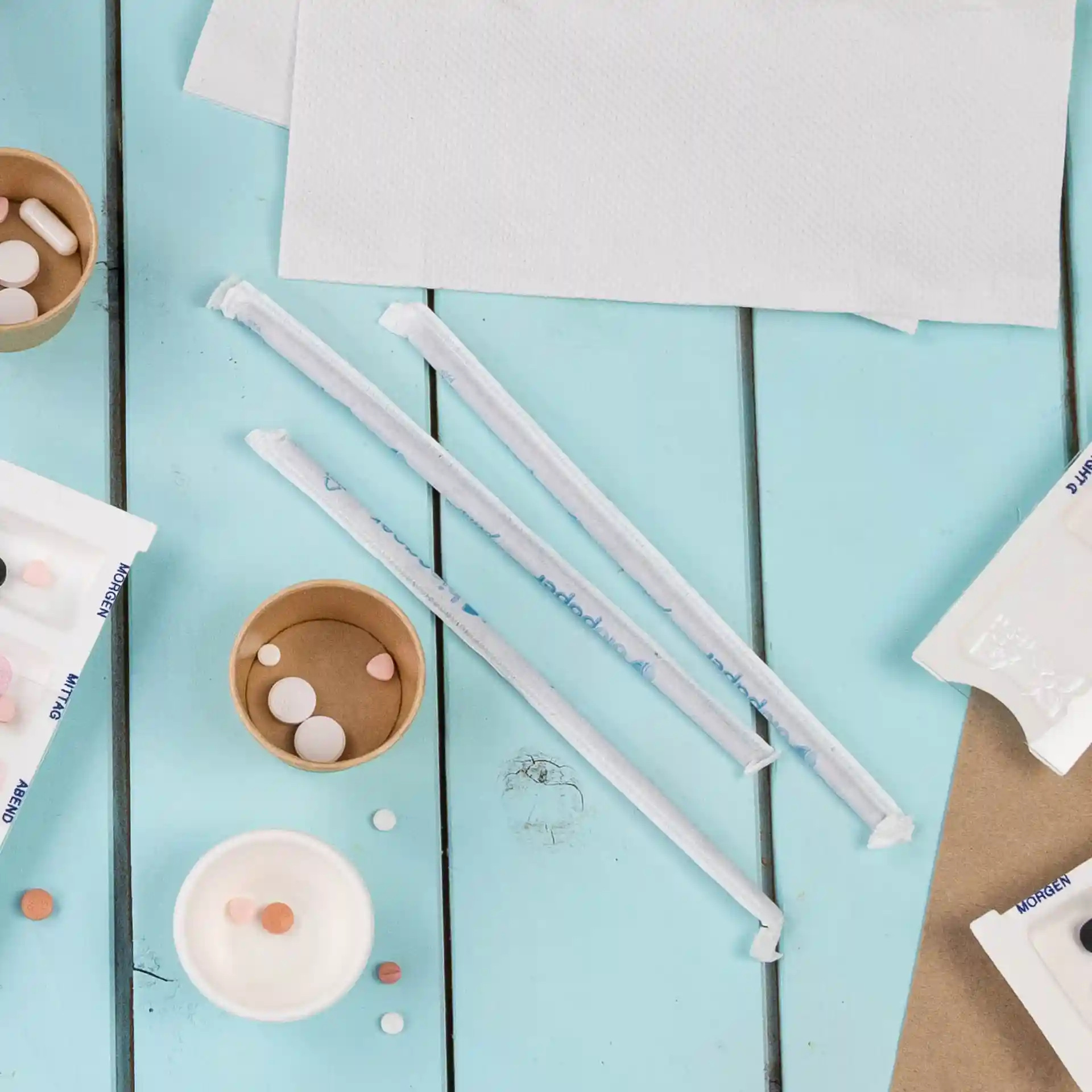 Pailles en papier noires flexibles, de 22 cm de long et 0,5 cm de diamètre, disposées avec des gobelets en papier et des bonbons sur une surface bleue.