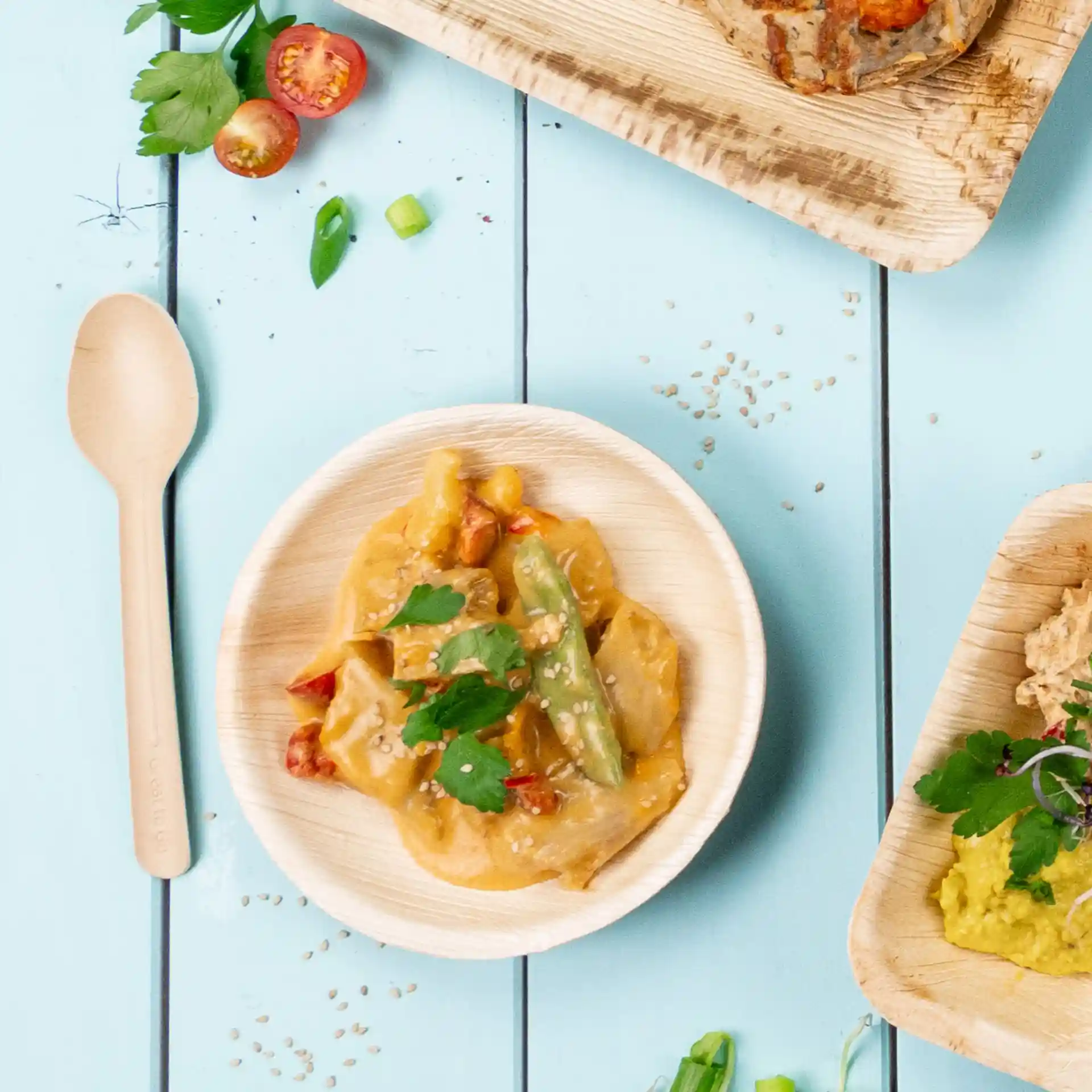 Bol de nourriture avec des légumes et une sauce, garni de coriandre, sur une surface bleu clair avec une cuillère en bois à proximité.