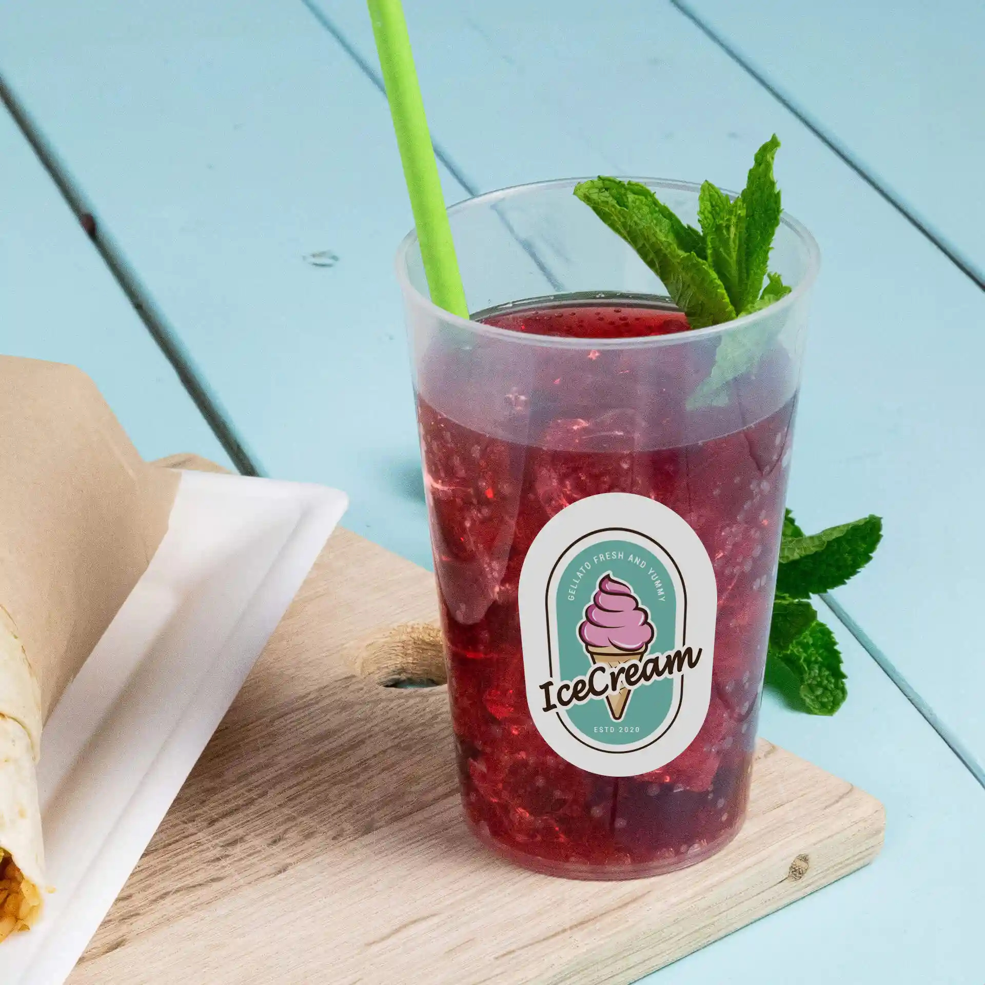 Gobelet réutilisable transparent avec un logo, rempli d'une boisson rouge et d'une paille verte, posé sur une surface en bois.