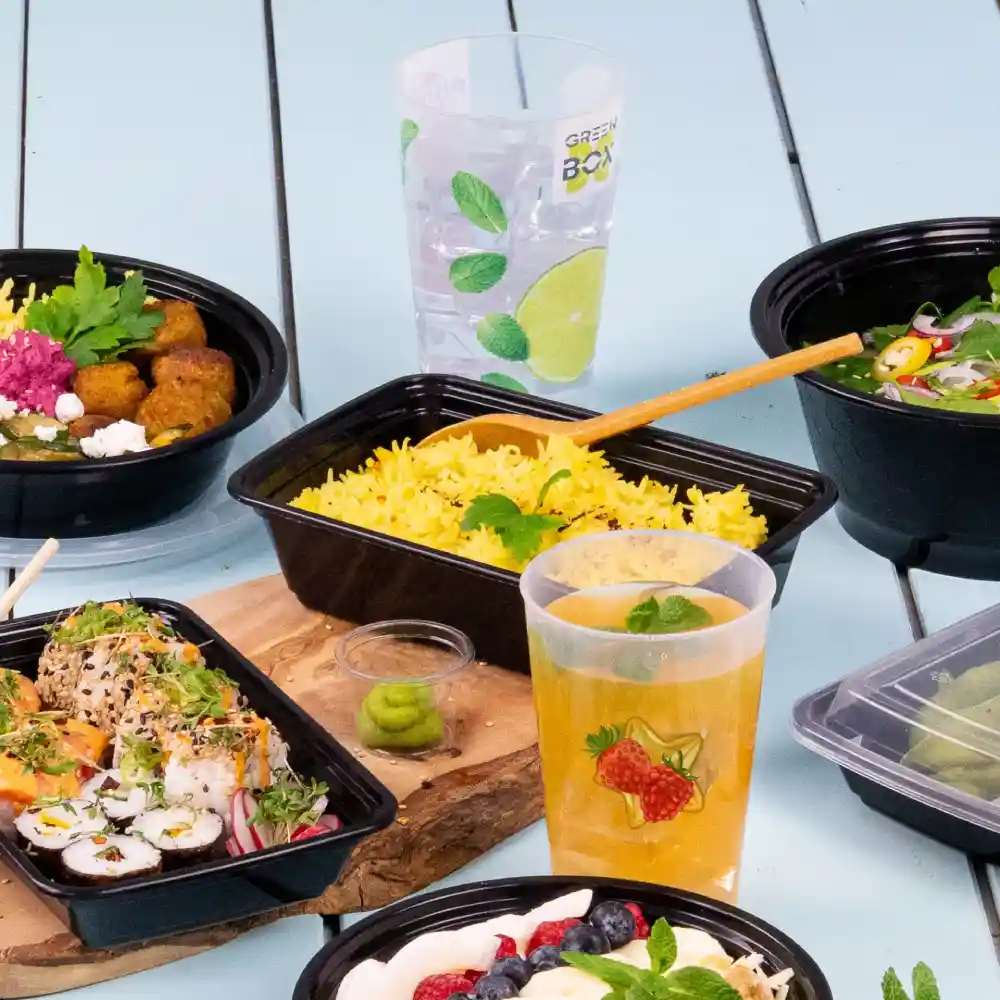 Contenants variés à emporter avec des aliments, y compris du riz, des sushis, des salades et des boissons sur une table bleue.