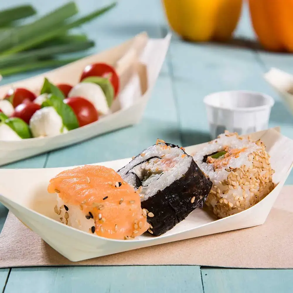 Rouleaux de sushi servis dans un plat en forme de bateau en bois, avec saumon, sésame et nori, accompagnés de tomates cerises et de mozzarella.