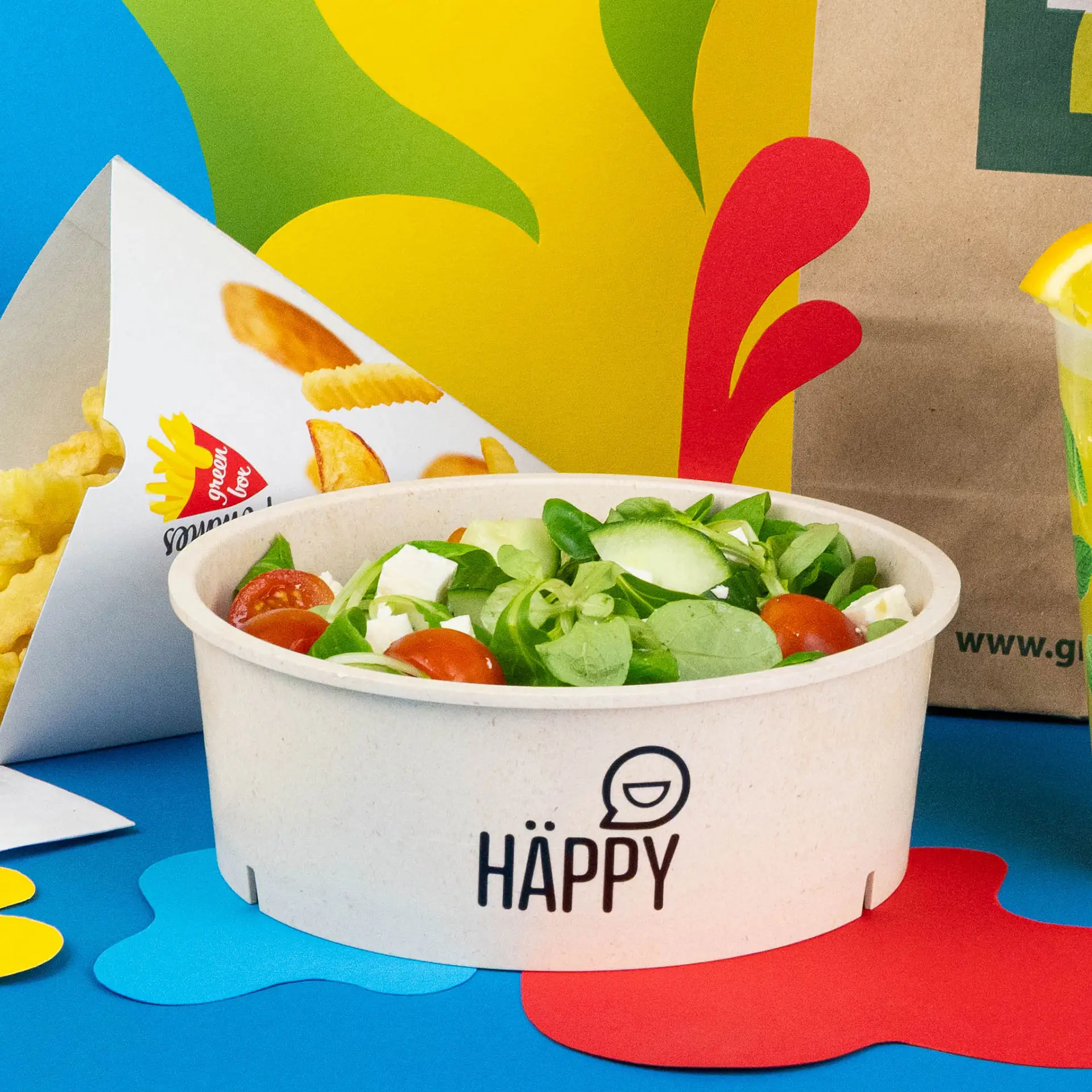 Bol réutilisable crème blanc rempli de salade comprenant de la laitue, des tomates et de la feta, avec un branding imprimé sur le côté.