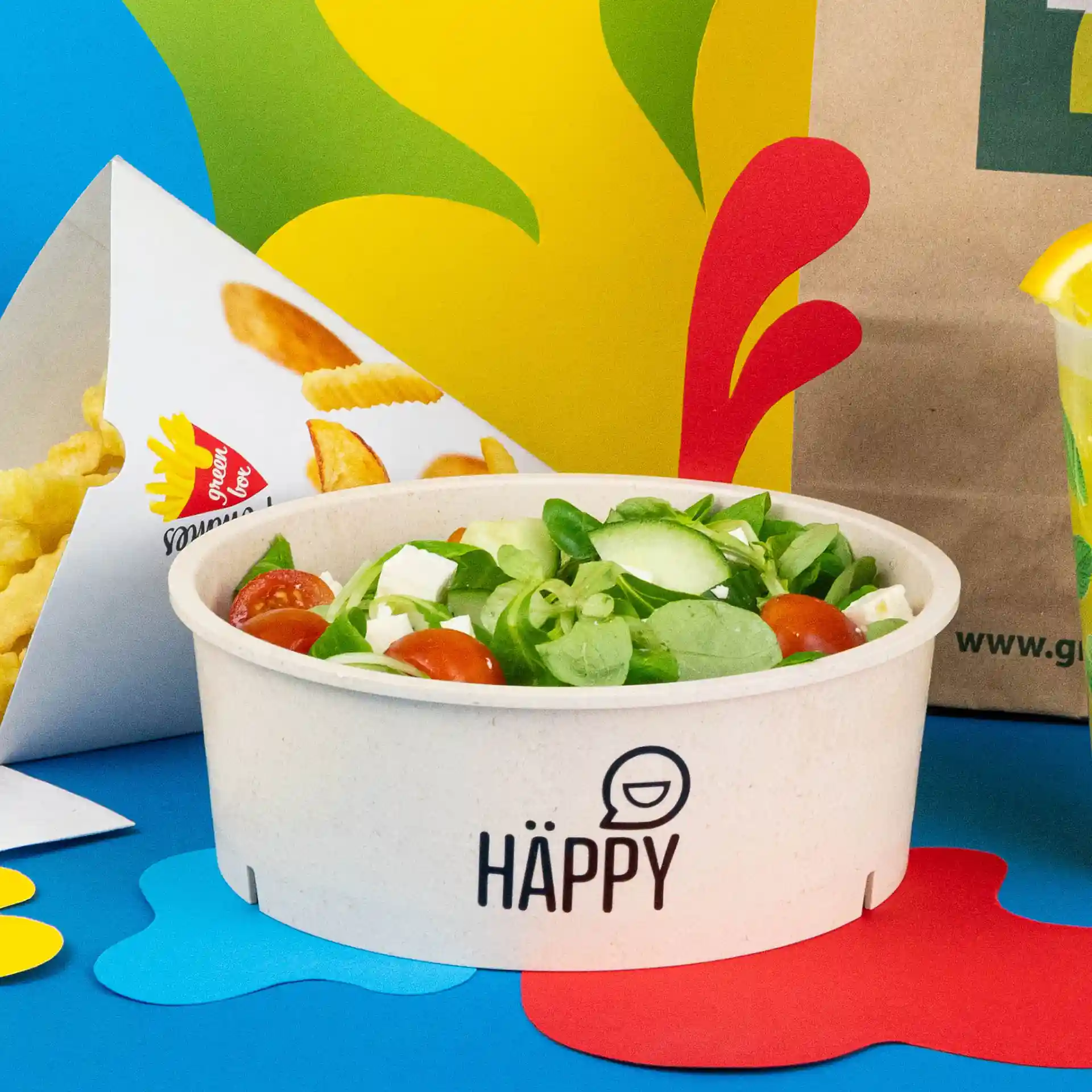 Bol rond réutilisable avec salade, couleur crème-blanc, sur un fond bleu avec d'autres aliments.