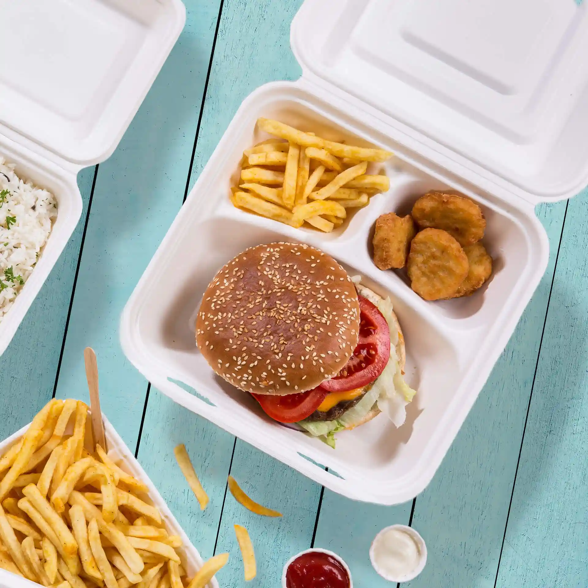 Image d'un conteneur en canne à sucre blanc avec trois compartiments, contenant un burger, des frites et des nuggets de poulet.
