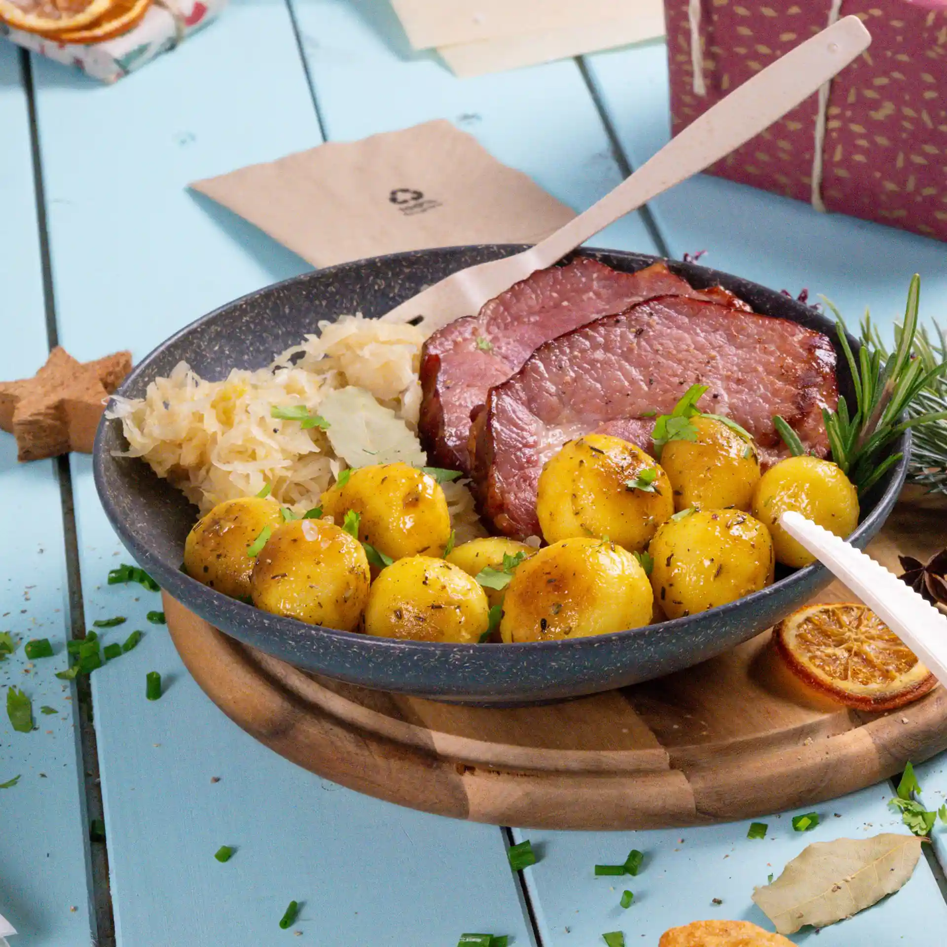 Assiette ronde grise profonde avec viande tranchée, pommes de terre bouillies et choucroute, posée sur une planche en bois.