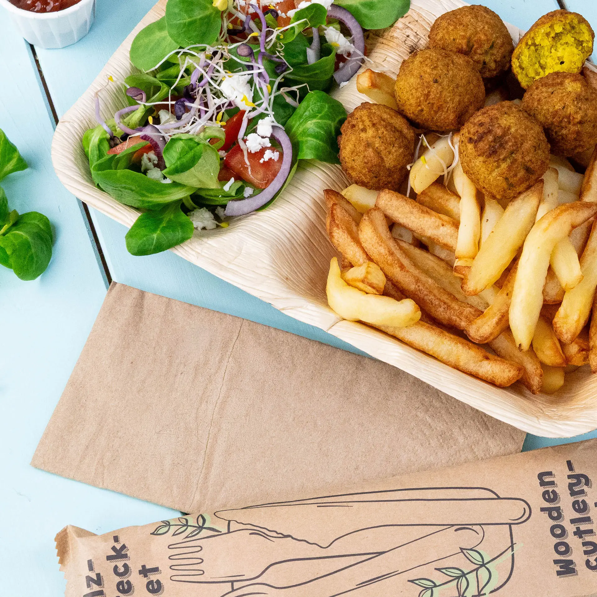 Image d'un plateau en bois contenant des boulettes de falafel, des frites et une salade mixte avec des légumes verts, des tomates et des oignons.