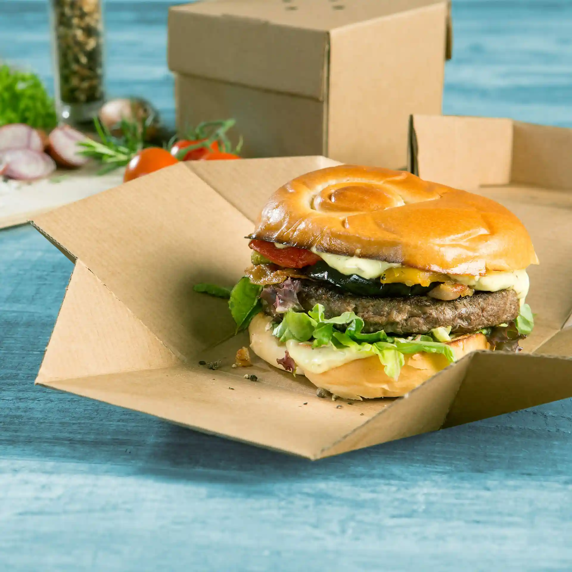 Burger dans une boîte en carton marron pliable, avec de la laitue, du fromage, du bacon et un pain moelleux.