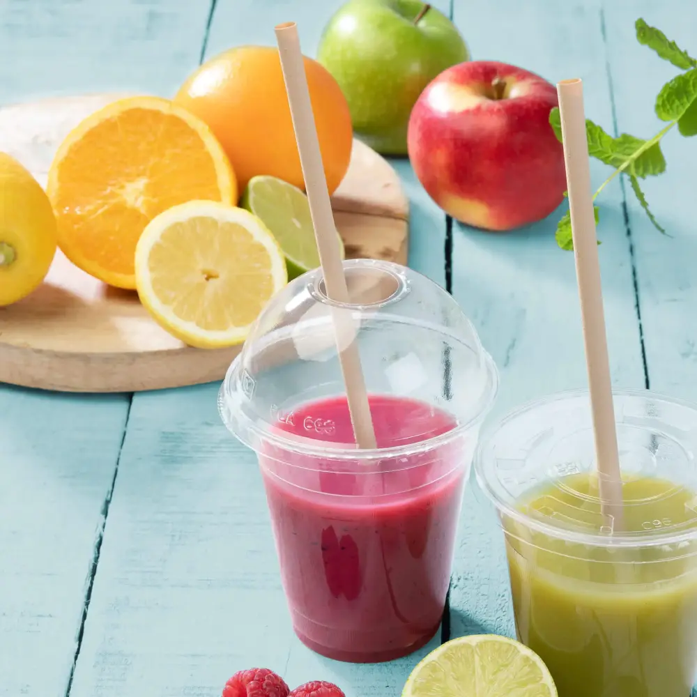 Deux gobelets transparents avec des smoothies aux fruits, un rose et un vert, placés à côté de fruits frais sur une surface bleue.