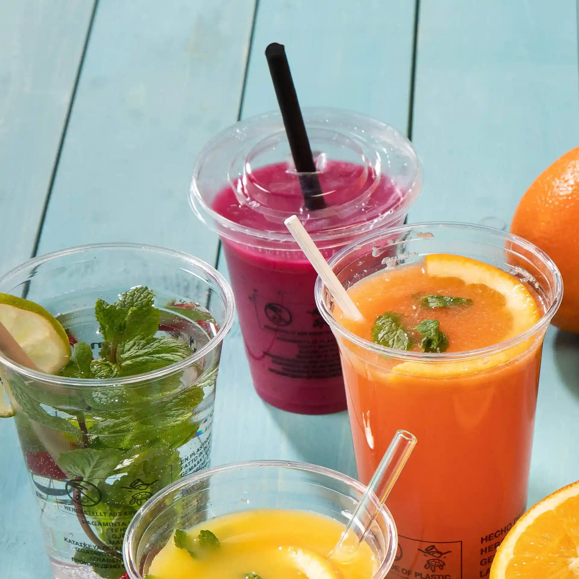 Image de plusieurs verres transparents avec des boissons : eau à la menthe, jus d'orange à la menthe et une boisson rose, sur une surface bleue.