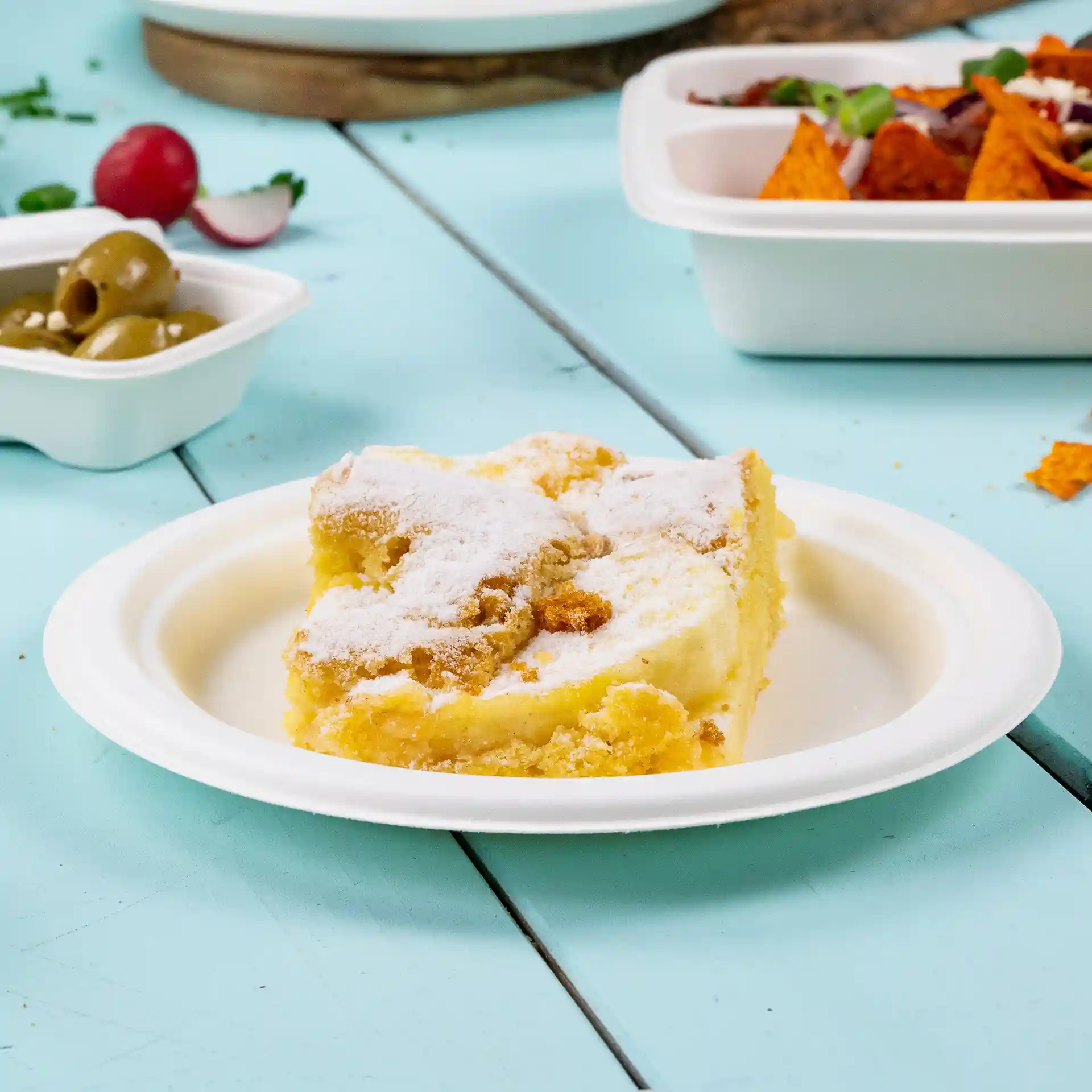 Partie de gâteau sur une assiette ronde en canne à sucre, saupoudrée de sucre glace, posée sur une surface en bois bleu.