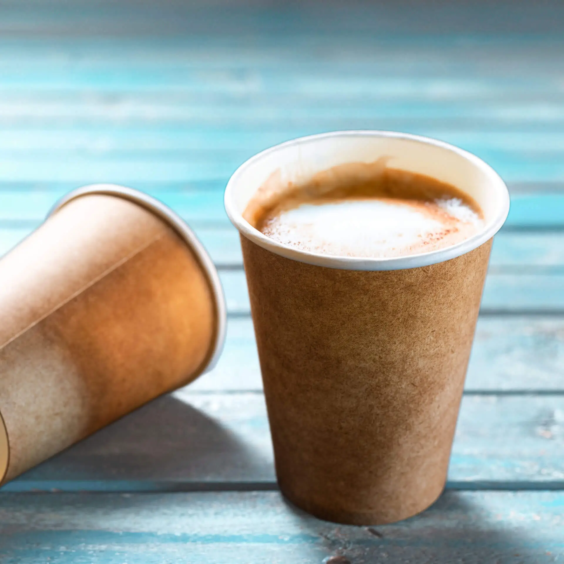 Gobelet en papier marron à paroi simple avec doublure blanche, rempli de café ; un autre gobelet est visible derrière.