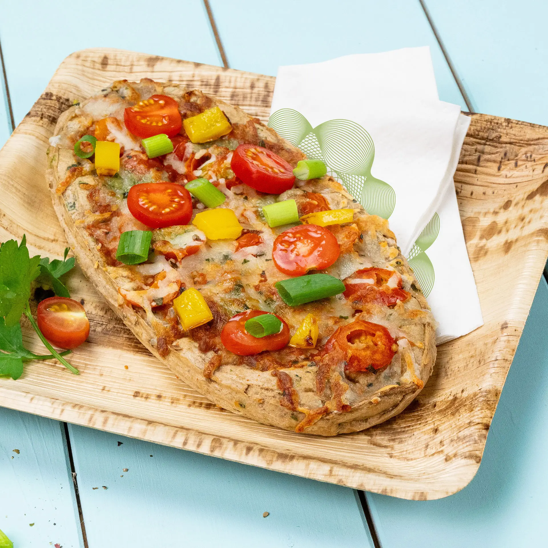 Pizza végétarienne garnie de tomates cerises, poivrons et oignons verts sur une assiette en bois avec une serviette.