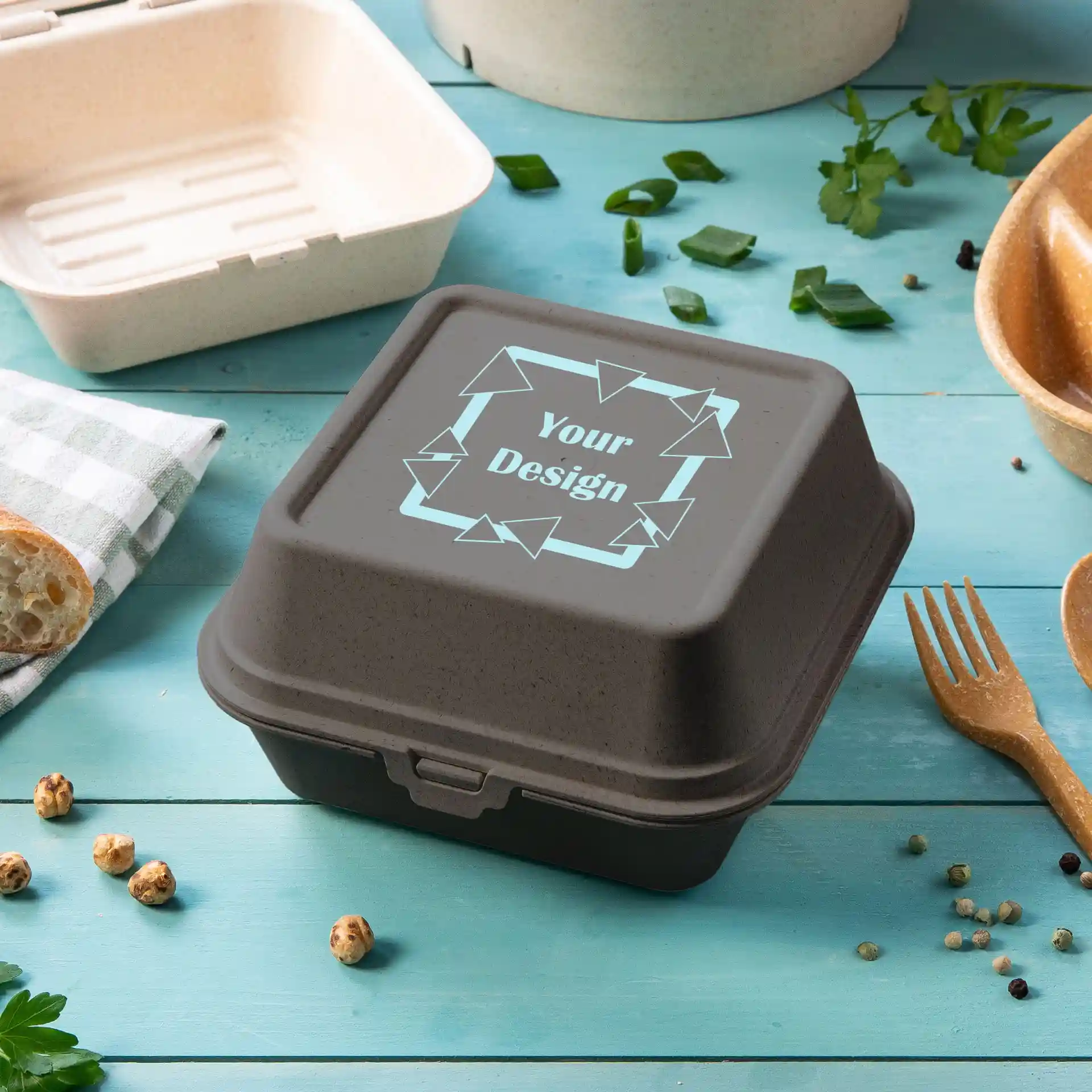 Boîte à burger rectangulaire grise avec couvercle, présentant une zone de design, placée sur une surface bleue avec des aliments autour.