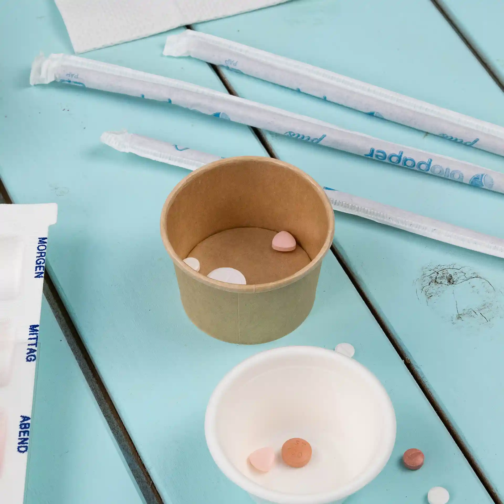 Conteneur rond en carton brun avec plusieurs petites pilules colorées à l'intérieur, placé sur une surface bleue.