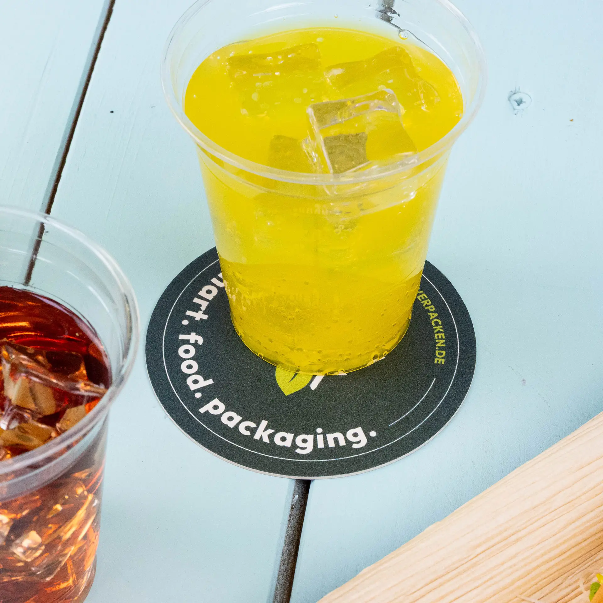 Boisson jaune dans un verre transparent sur un dessous de verre rond imprimé avec texte, à côté d'un verre de boisson sombre avec des glaçons.