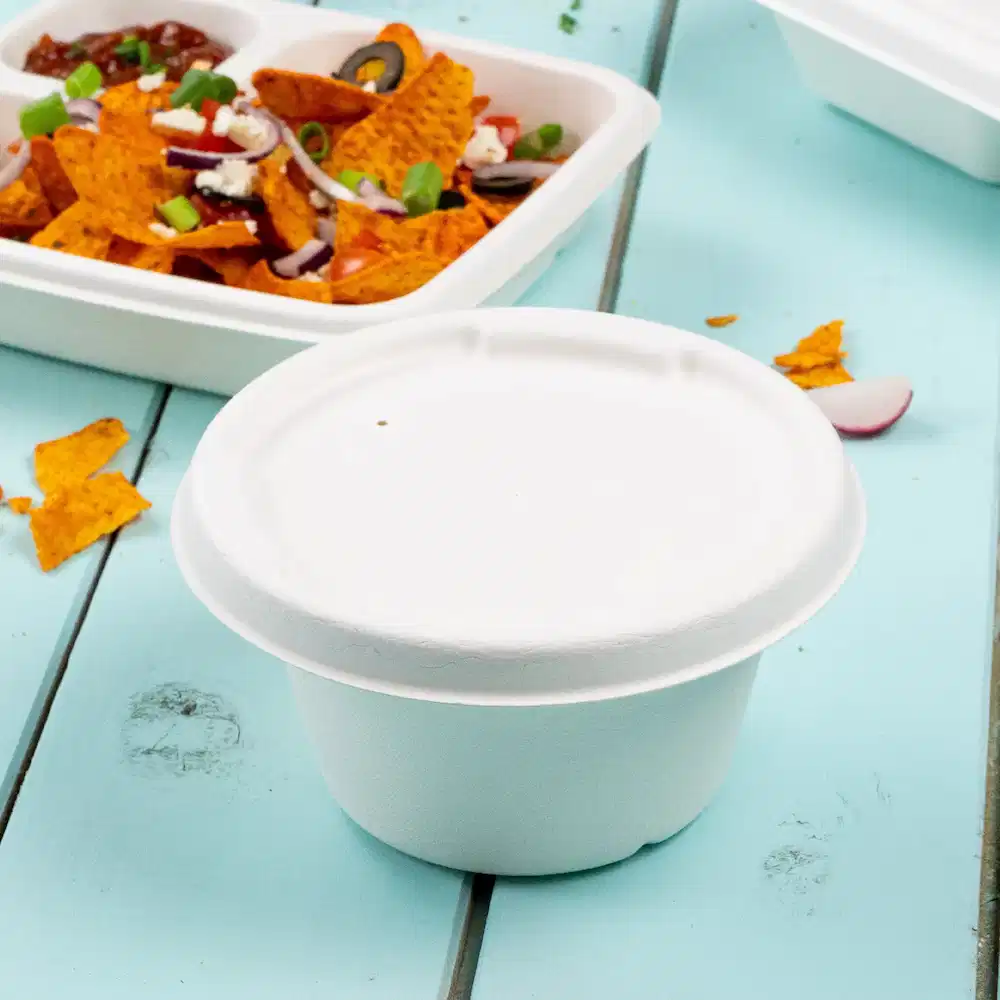 Gobelet en papier blanc pour soupe sur une table bleue avec en arrière-plan des nachos et un contenant alimentaire scellé.