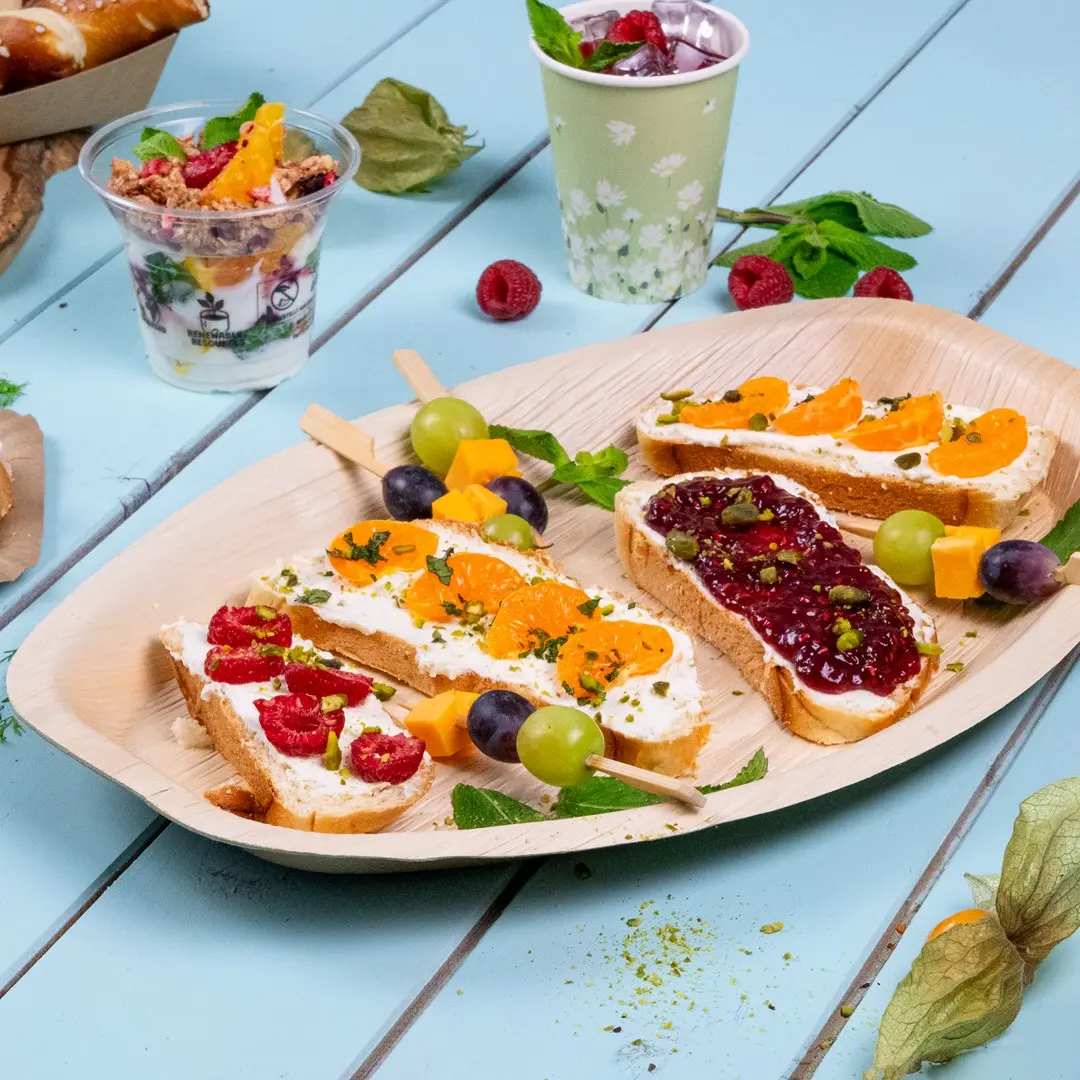 Plateau avec divers amuse-bouches, y compris du pain garni de fromage à la crème, des fruits et une brochette de fruits, accompagné d'un parfait au yaourt.