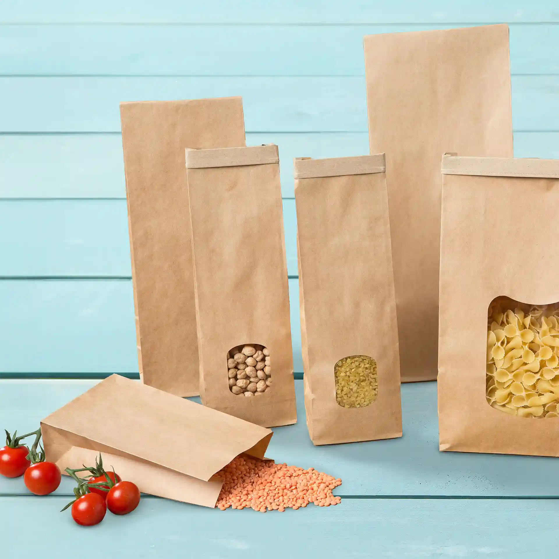 Sacs en papier kraft marron de différentes tailles avec un design simple, certains contenant des lentilles et des pâtes, sur un fond bleu.