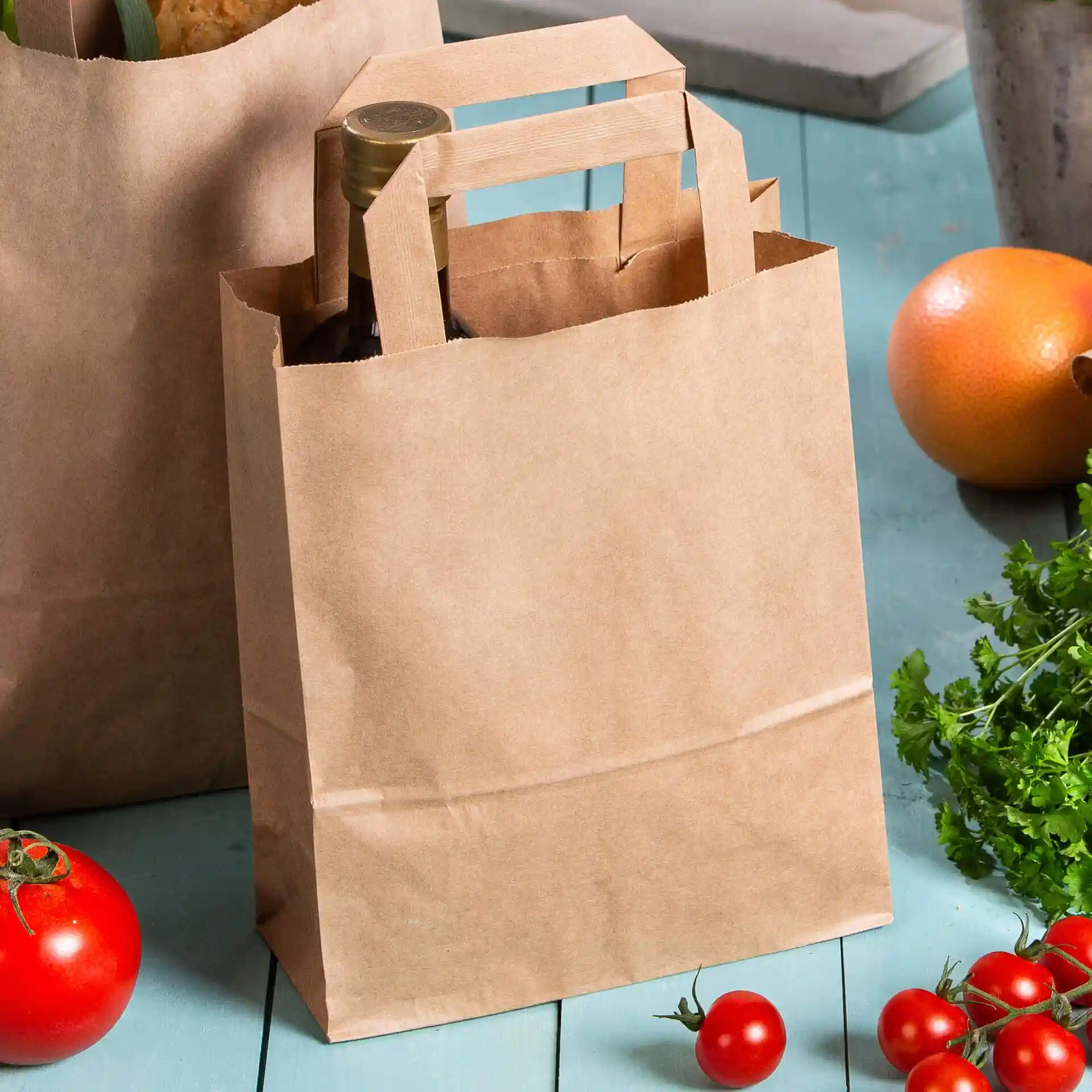 Sac en papier brun avec poignées, contenant une bouteille, entouré de tomates et d'autres produits.
