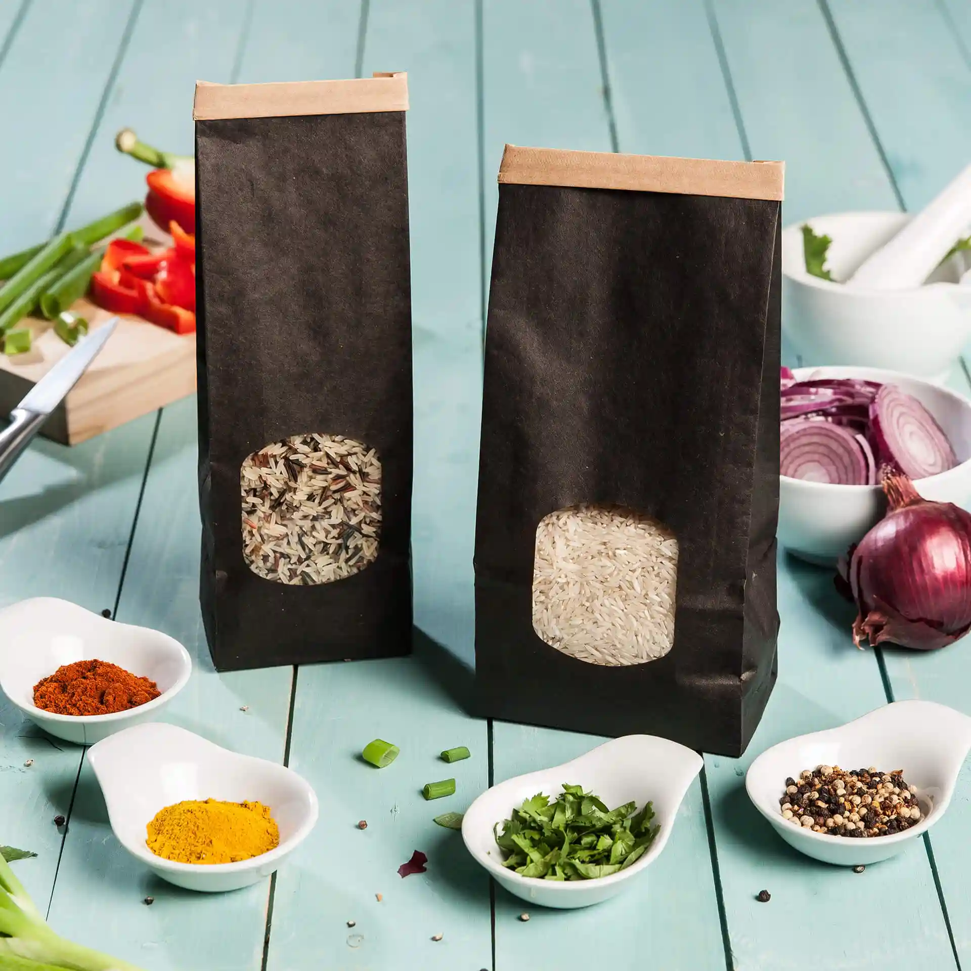 Deux sacs noirs à fond plat avec fenêtres de visualisation, l'un rempli de riz mélangé et l'autre de riz blanc, sur une surface en bois bleu.