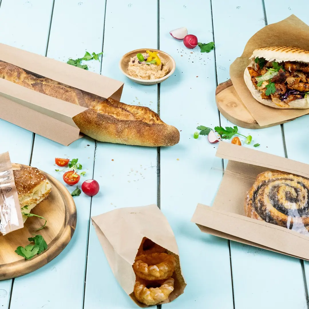 Image de diverses pâtisseries, y compris une baguette, un sandwich, des viennoiseries et un bol de dip sur une surface en bois bleu.