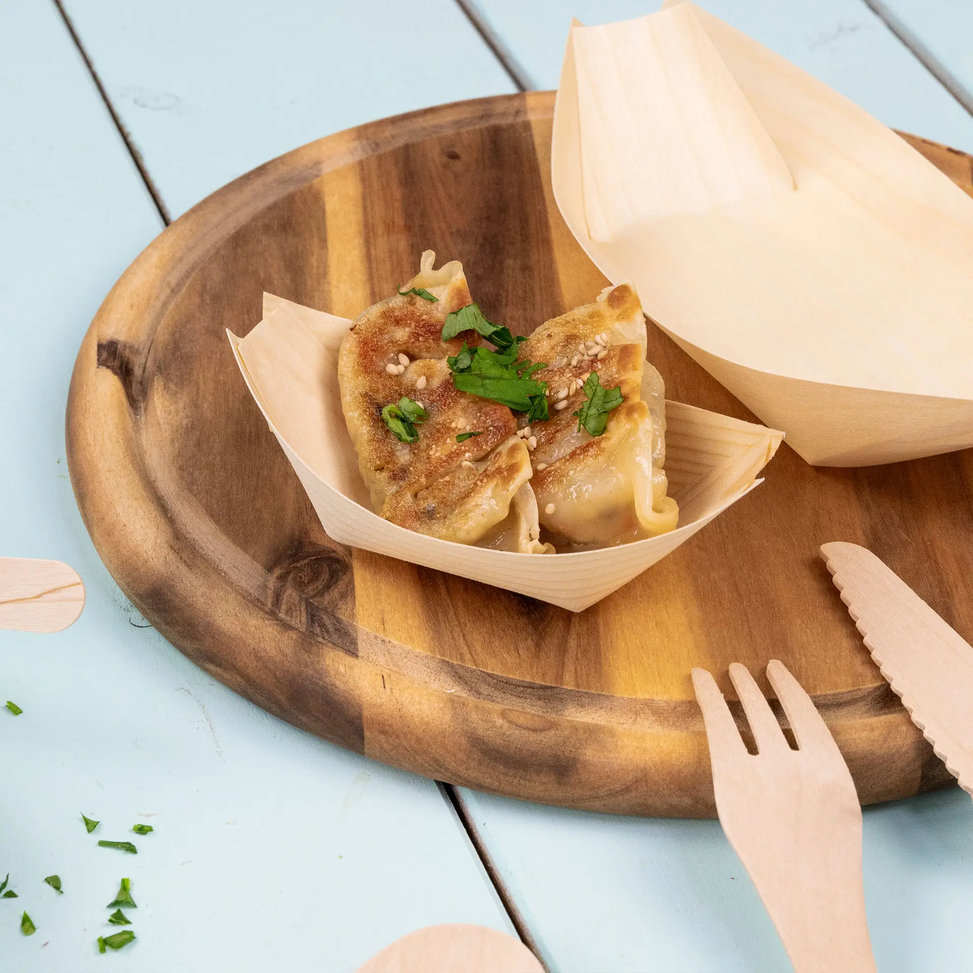 Conteneur en forme de bateau en bois avec deux raviolis garnis de sésame et de persil sur un plateau en bois.