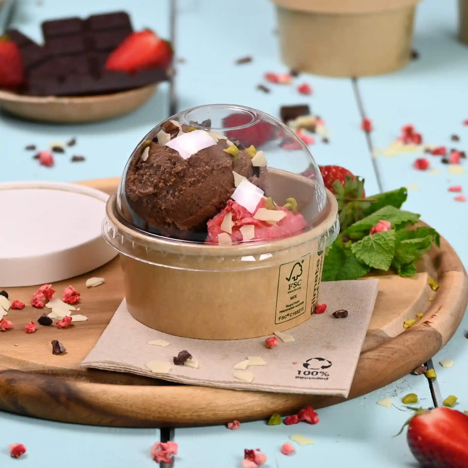 Contenant avec deux boules de glace, garni de noix et de noix de coco, sur une planche en bois avec de la menthe et des fraises.