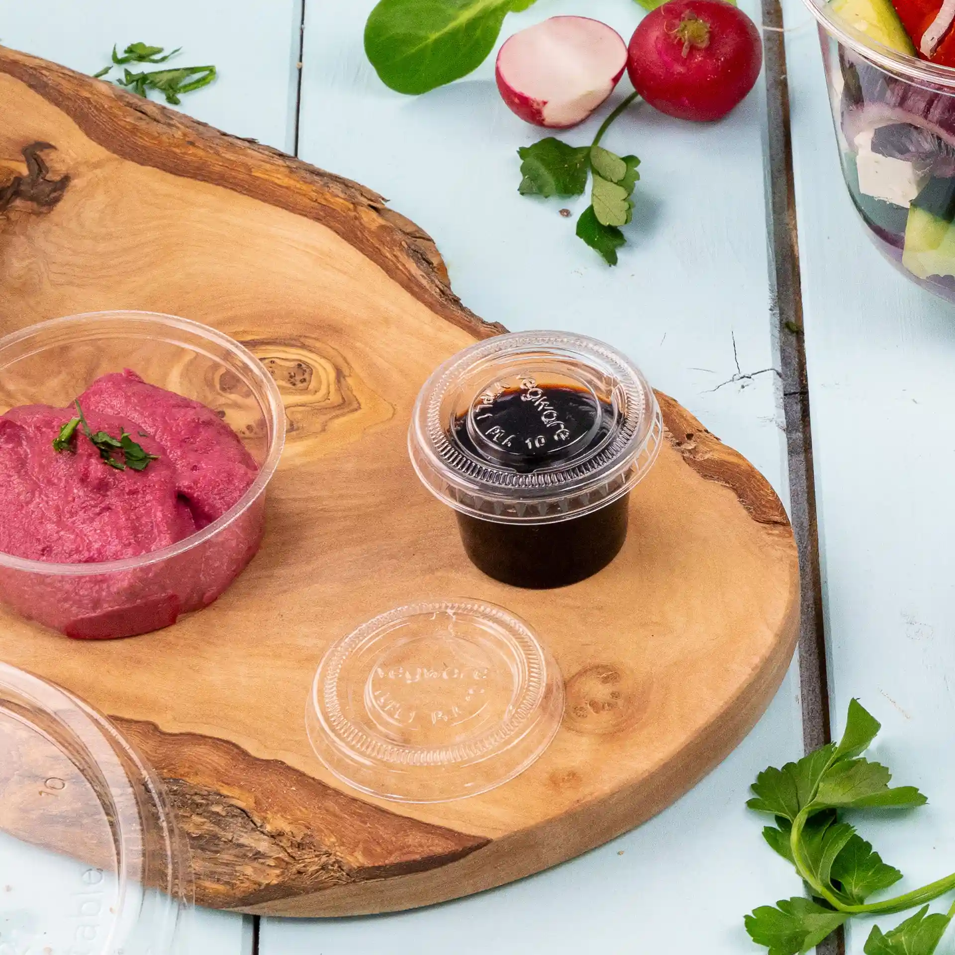 Image d'une planche de service en bois avec une trempette rose dans un récipient transparent et une sauce foncée dans un autre récipient transparent.