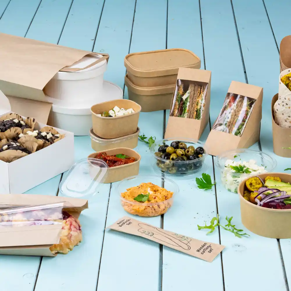 Un assortiment de contenants alimentaires comprend des boîtes en papier, des bols et des gobelets en plastique transparent avec divers plats et collations.