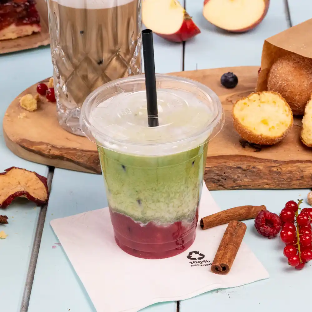 Boisson glacée en couches dans un gobelet transparent avec une paille, entourée de collations et d'une serviette sur une surface bleu clair.