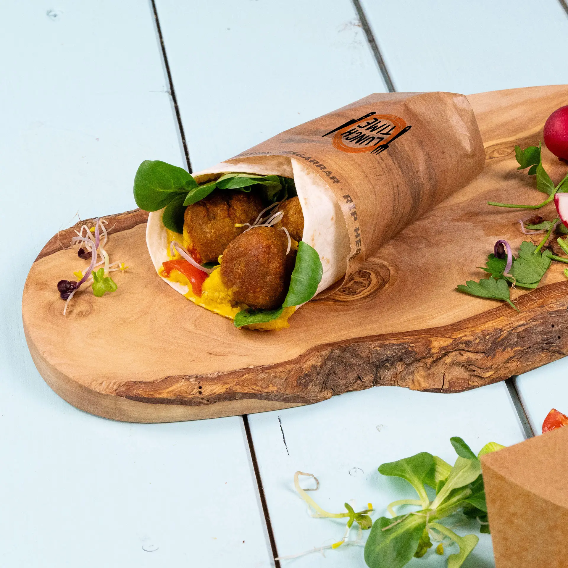 Un sac-emballage imprimé personnalisé contenant des falafels, des légumes et de la sauce, placé sur une planche en bois.