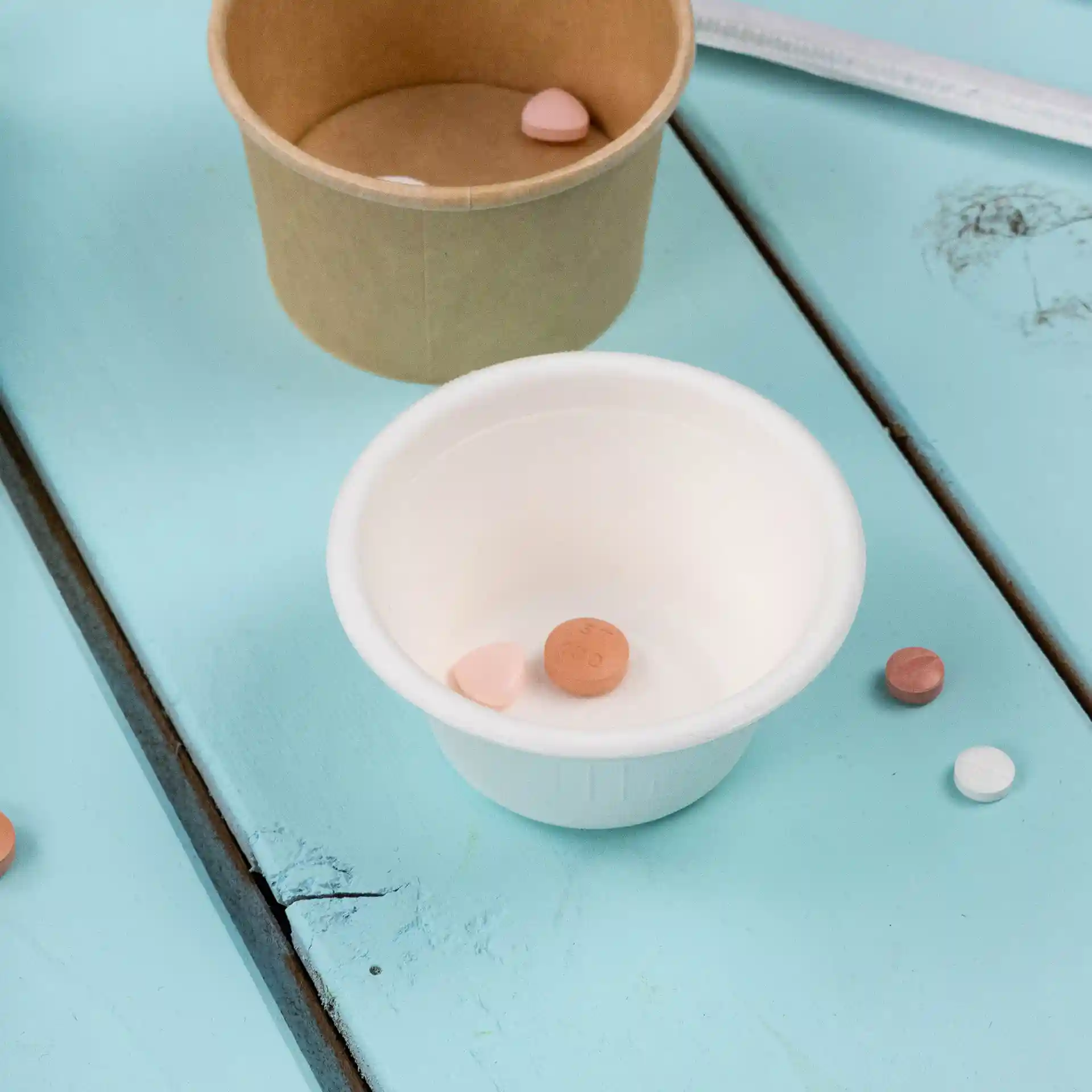 Bol en bagasse blanc de 62 mm de diamètre, contenant plusieurs petites pilules sur une surface en bois bleu.