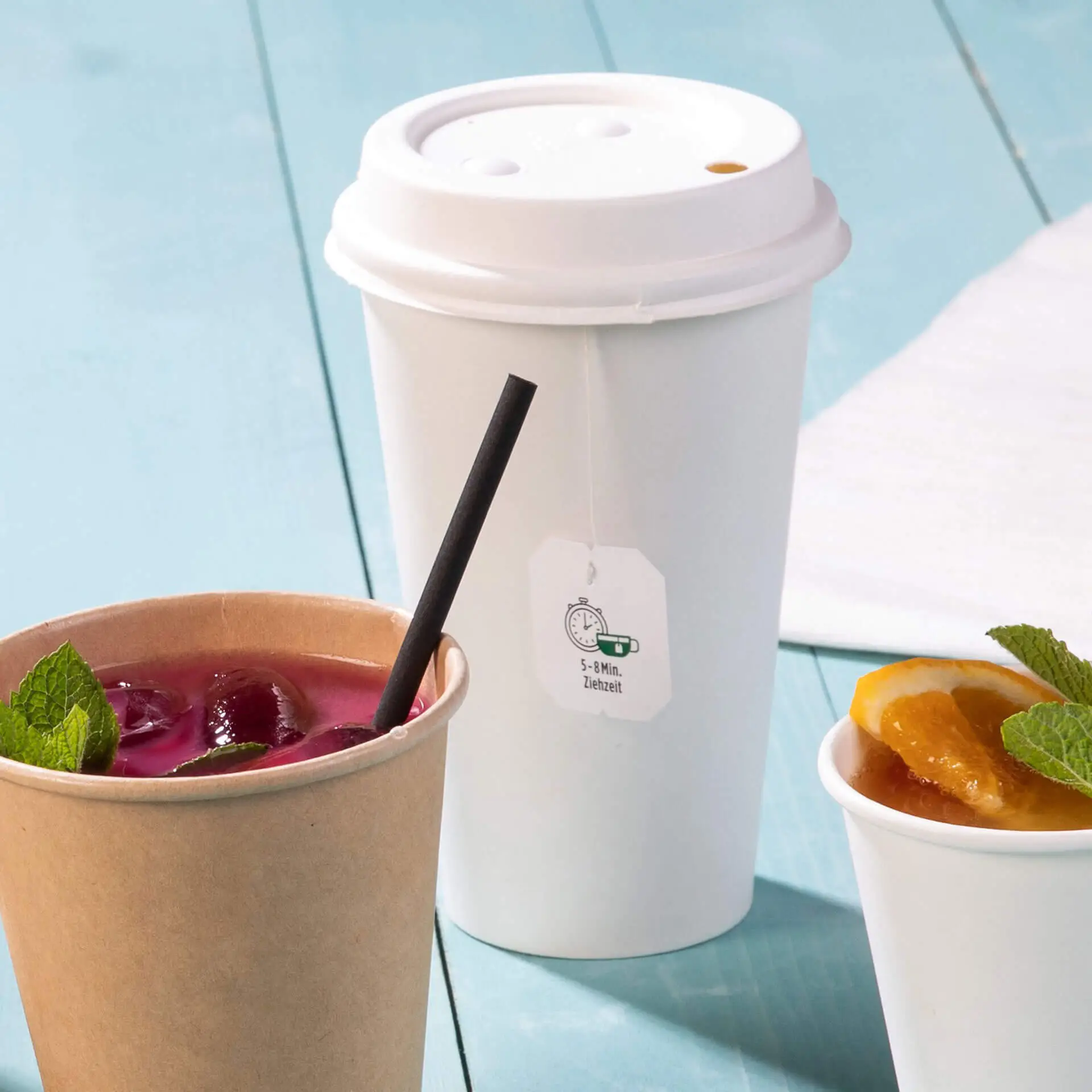 Gobelet en papier blanc à paroi simple avec revêtement PLA, à côté d'un gobelet en kraft contenant une boisson sombre et un garniture de fruits.