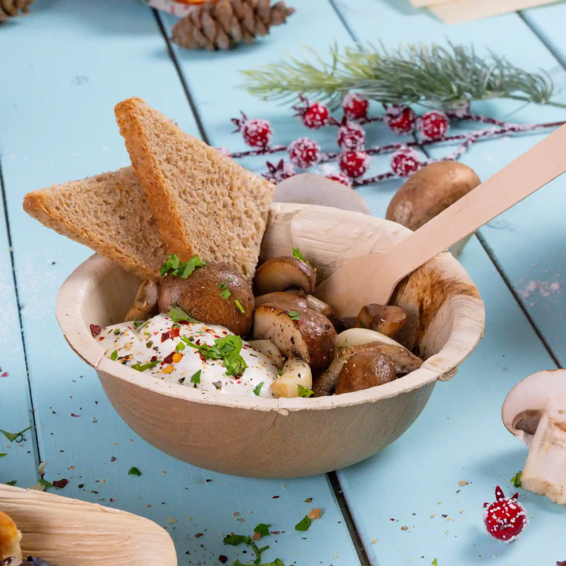 Bol en feuille de palmier contenant des champignons, une cuillerée de sauce et deux tranches de pain complet, avec une cuillère en bois.