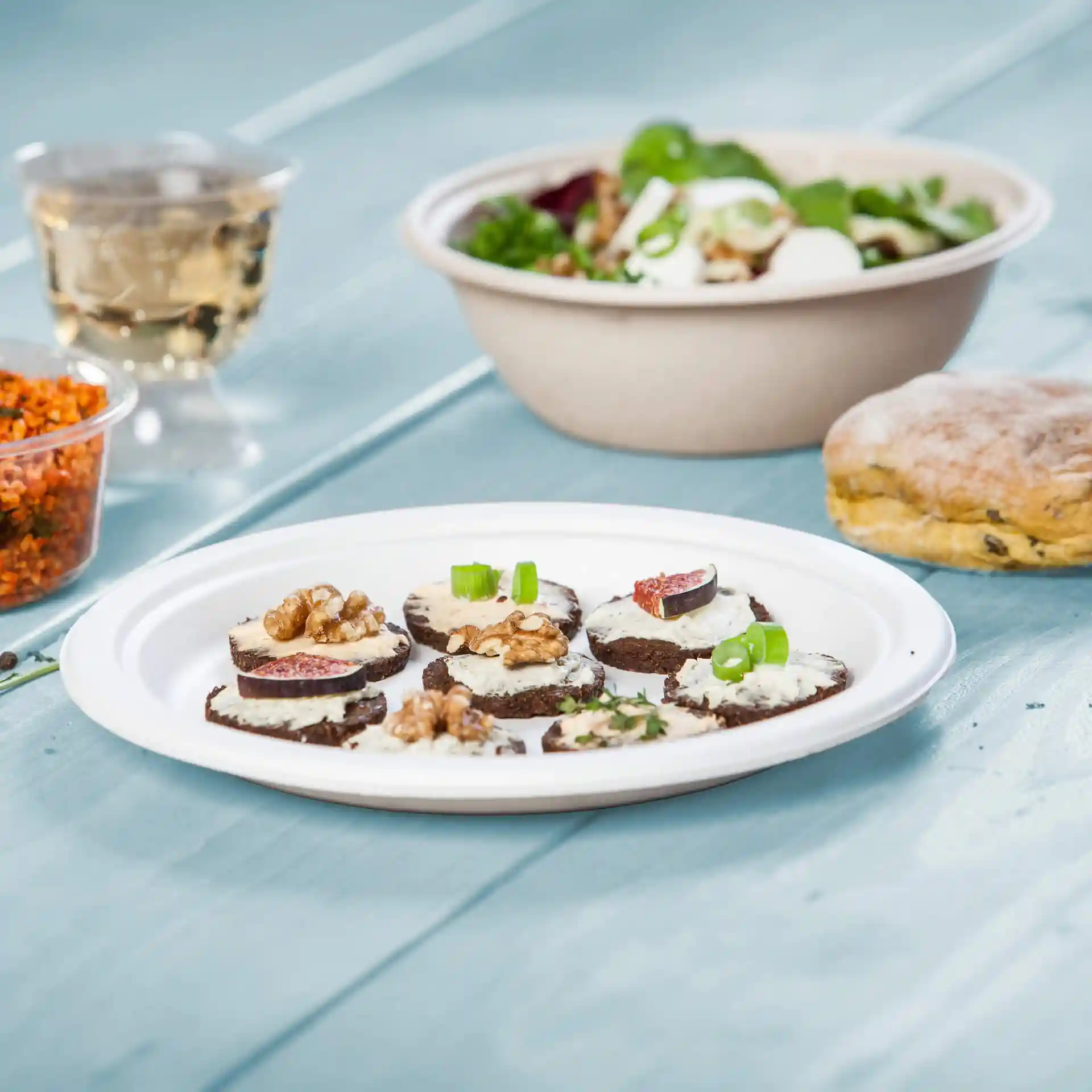 Assiette avec plusieurs tranches rondes de pain noir garnies de crème, noix et figues, accompagnées d'une salade et d'un biscuit.