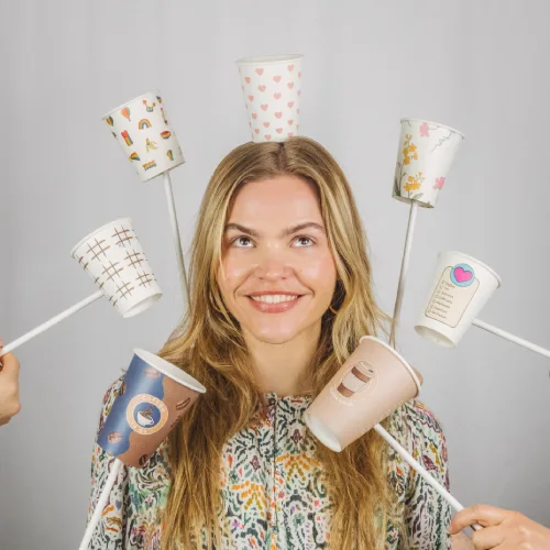 Femme avec de longs cheveux souriante, tenant plusieurs gobelets en papier colorés sur des bâtons autour de sa tête.