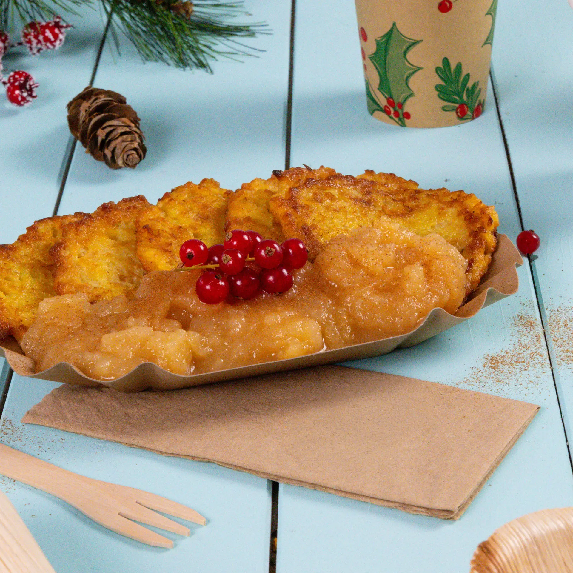 Assiette avec plusieurs beignets dorés, compote de pommes et groseilles rouges, sur une surface en bois bleu clair.