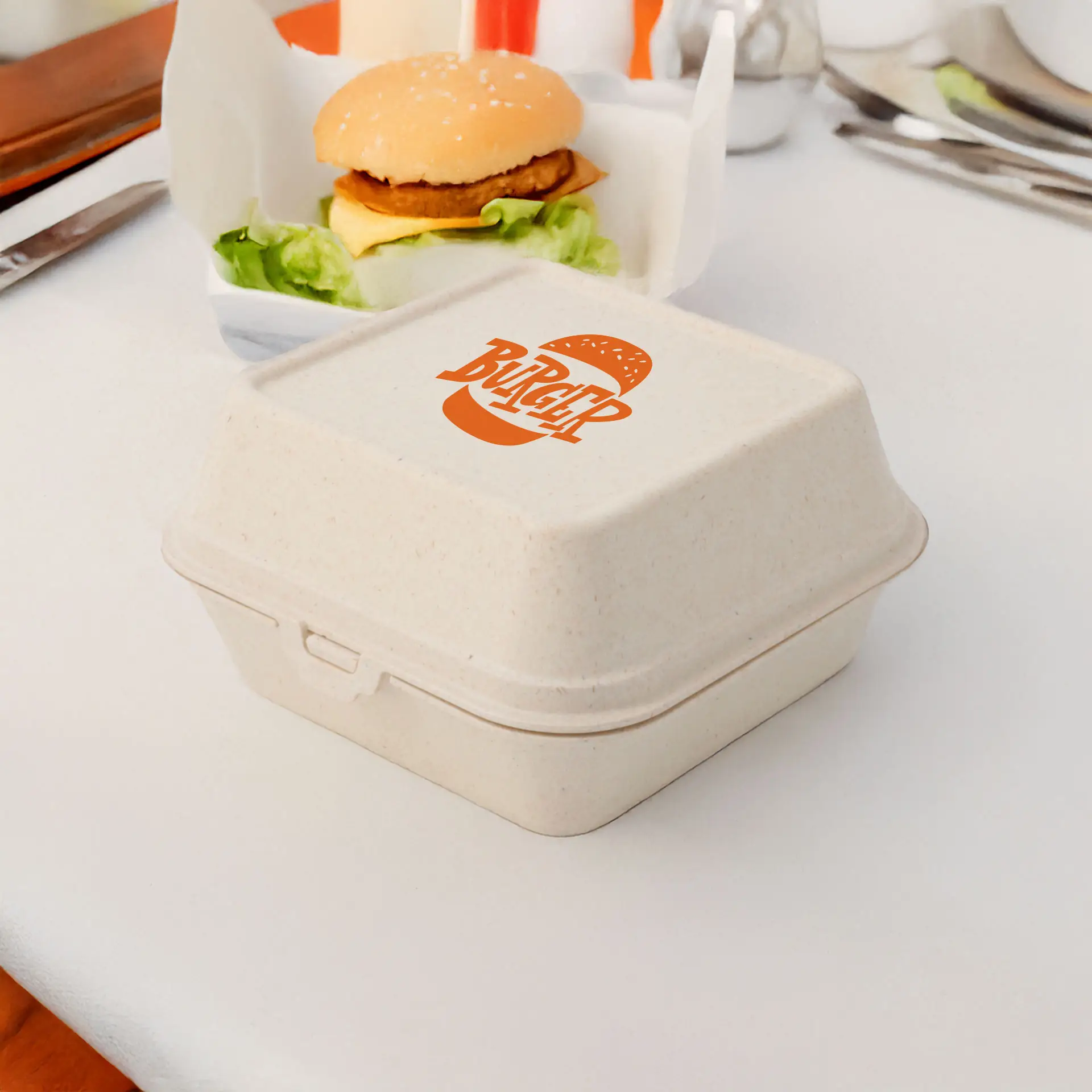 Boîte à burger réutilisable crème blanche avec logo imprimé, idéale pour aliments chauds et froids, placée à côté d'un burger sur une table.