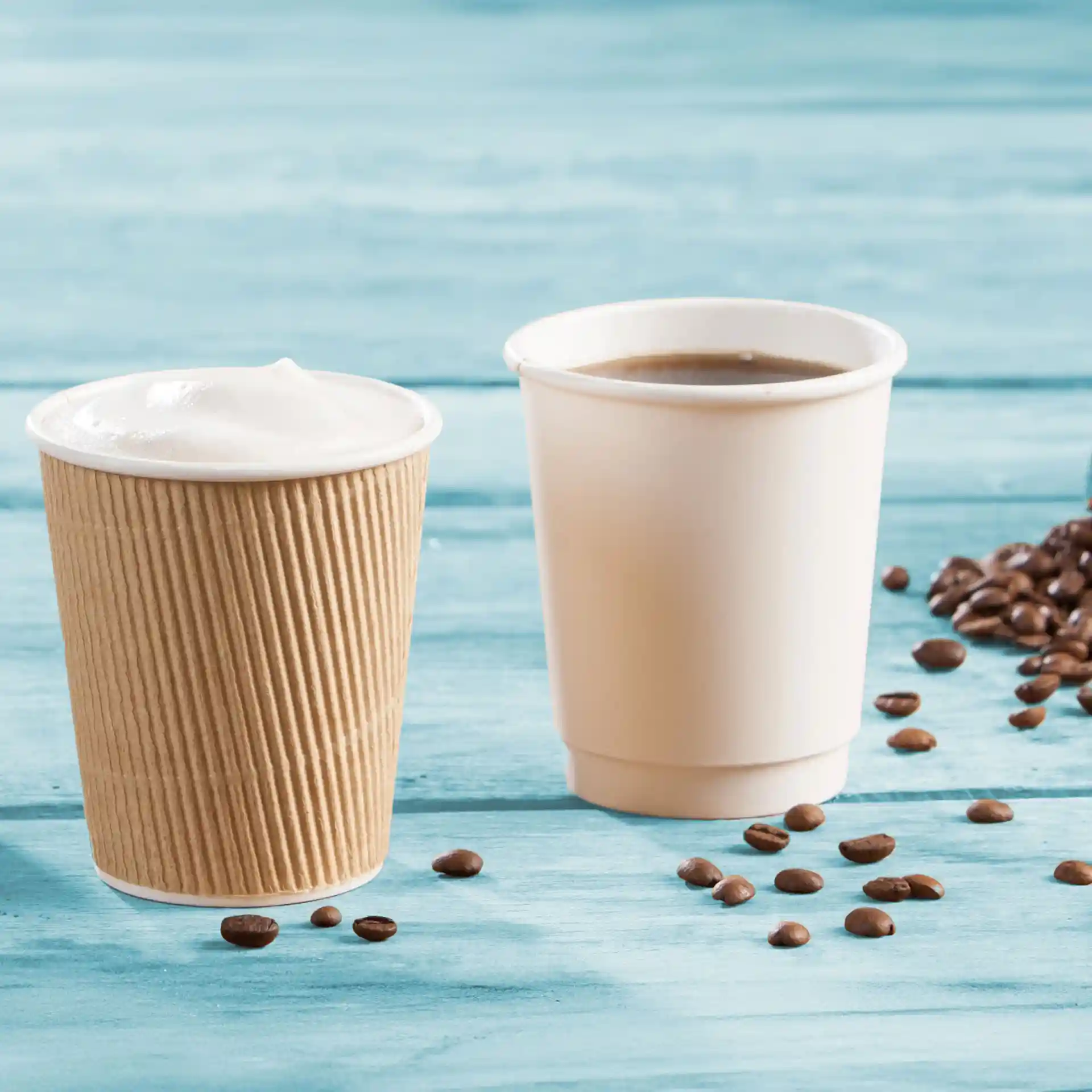 Gobelets en carton à double paroi marron et blanc, avec des grains de café éparpillés sur une surface en bois bleu.