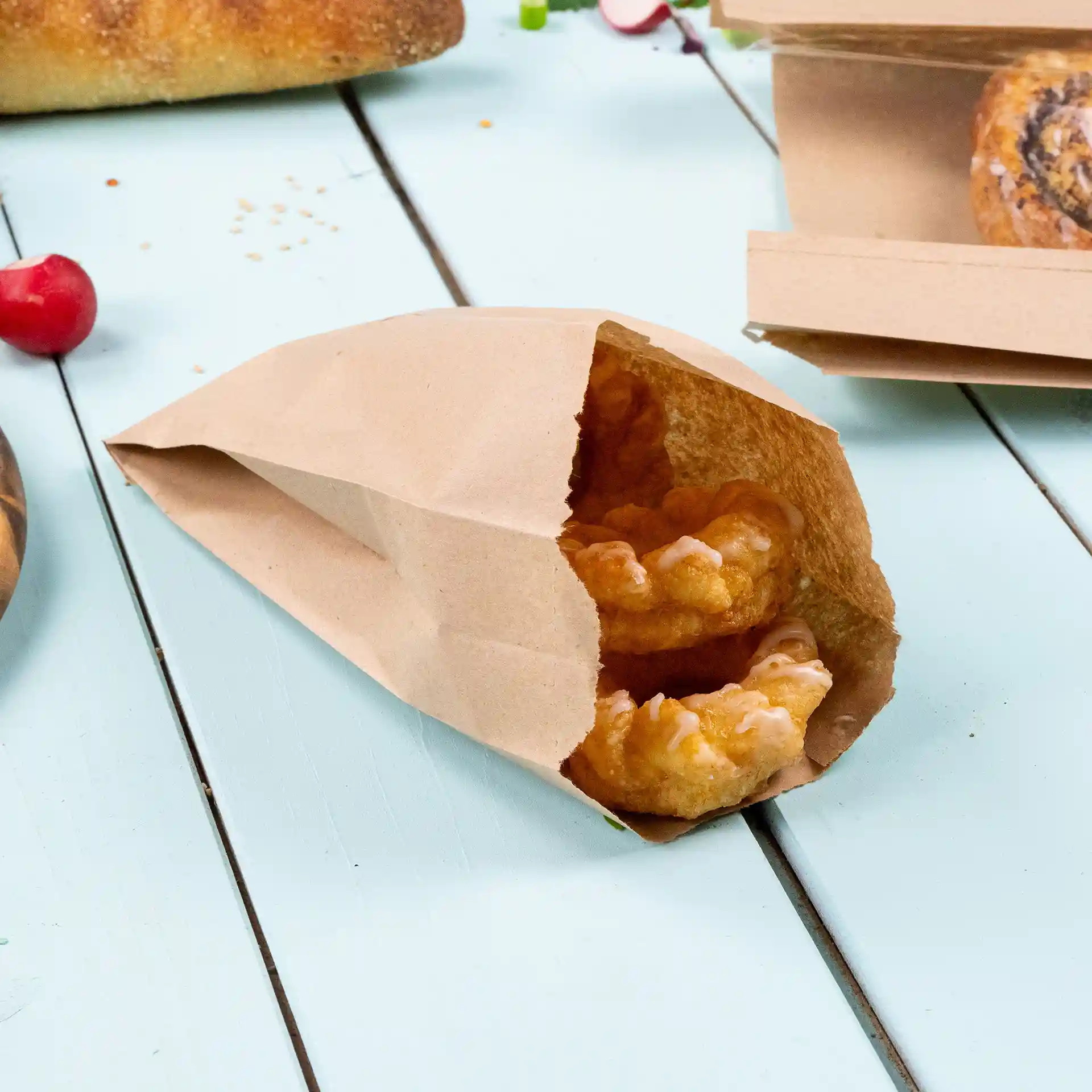 Sac en papier brun plat contenant deux pâtisseries, posé sur une surface en bois bleu clair.